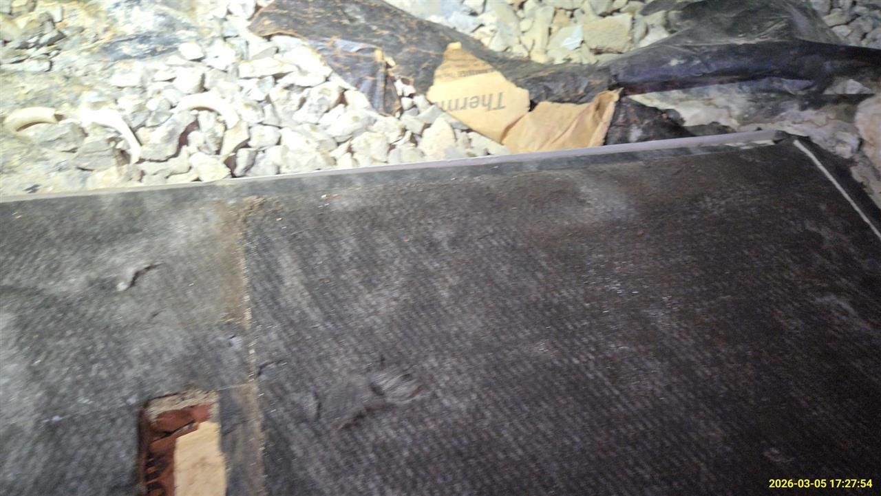 A dark, textured rectangular surface, possibly insulation or matting, lies next to gravel and a piece of cardboard.