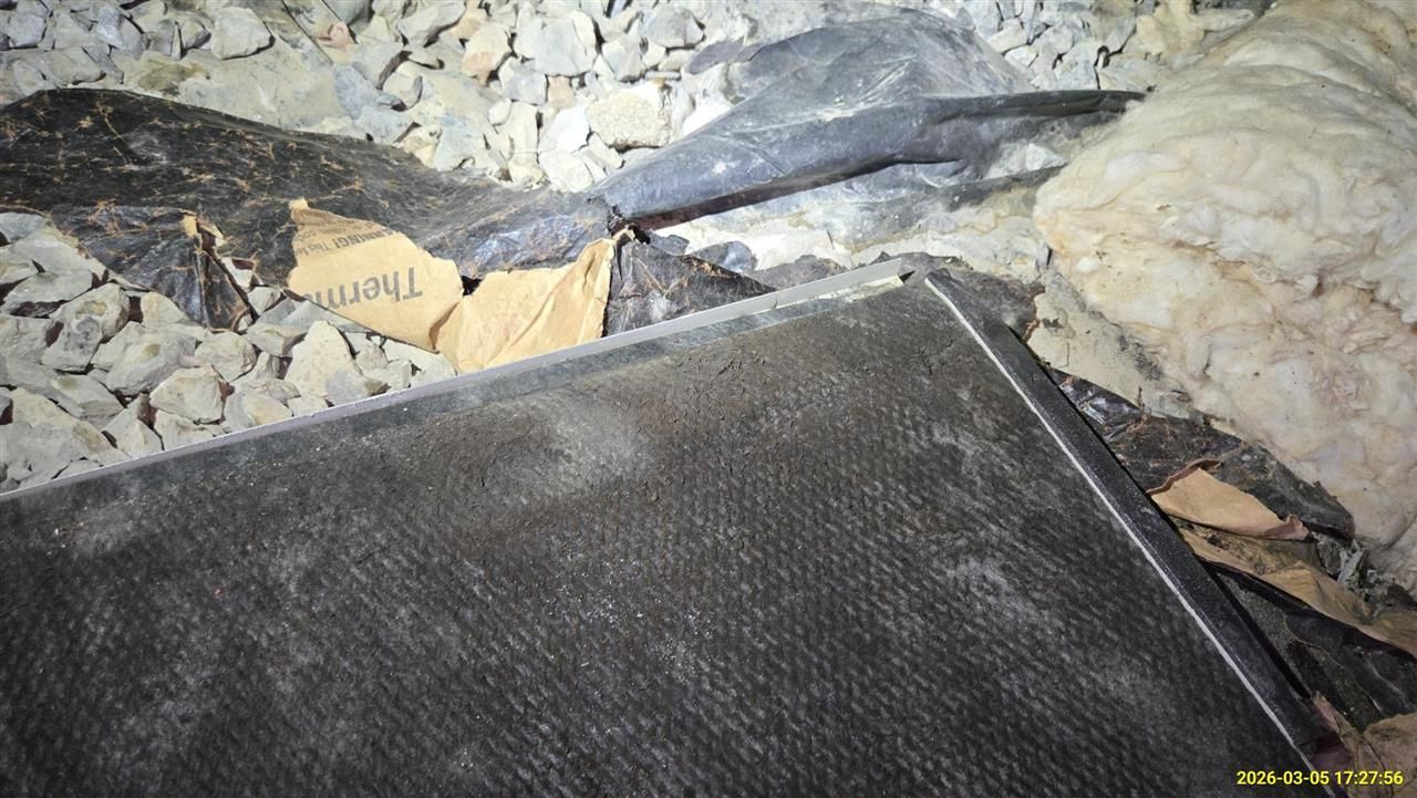 A dark HVAC filter sits in a dusty attic near loose insulation and a piece of paper labeled Therm.