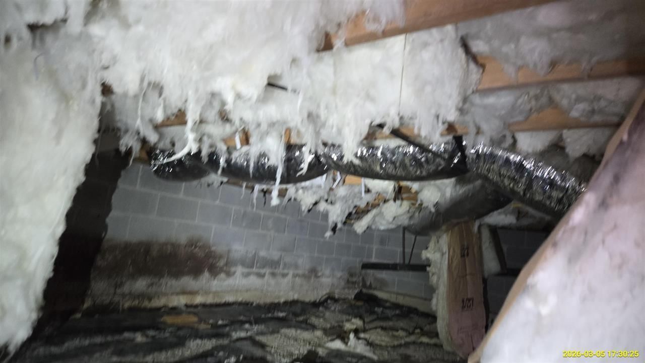 A dimly lit crawl space with sagging fiberglass insulation hanging from wooden floor joists and silver ductwork.