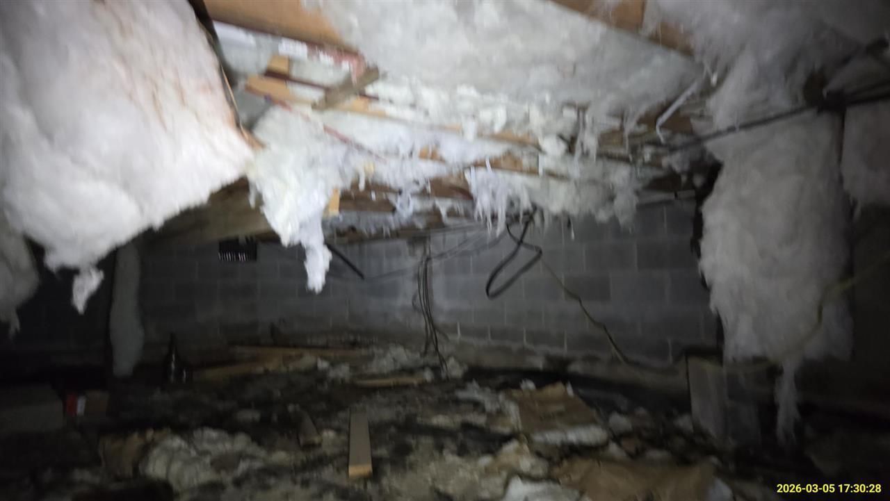 A crawlspace featuring sagging, damaged fiberglass insulation hanging from ceiling joists over a dark, debris-filled floor.