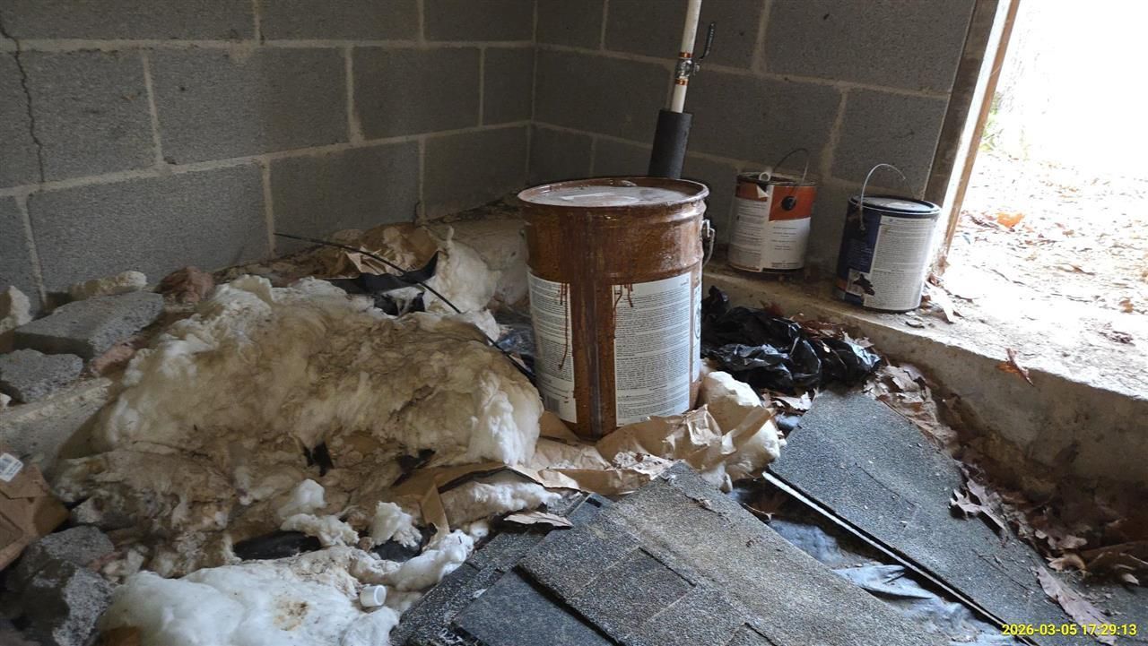 Debris, old insulation, and paint cans in the corner of a basement with concrete block walls.