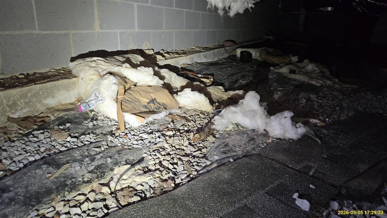 Debris and torn insulation scattered on the ground next to a concrete block wall.