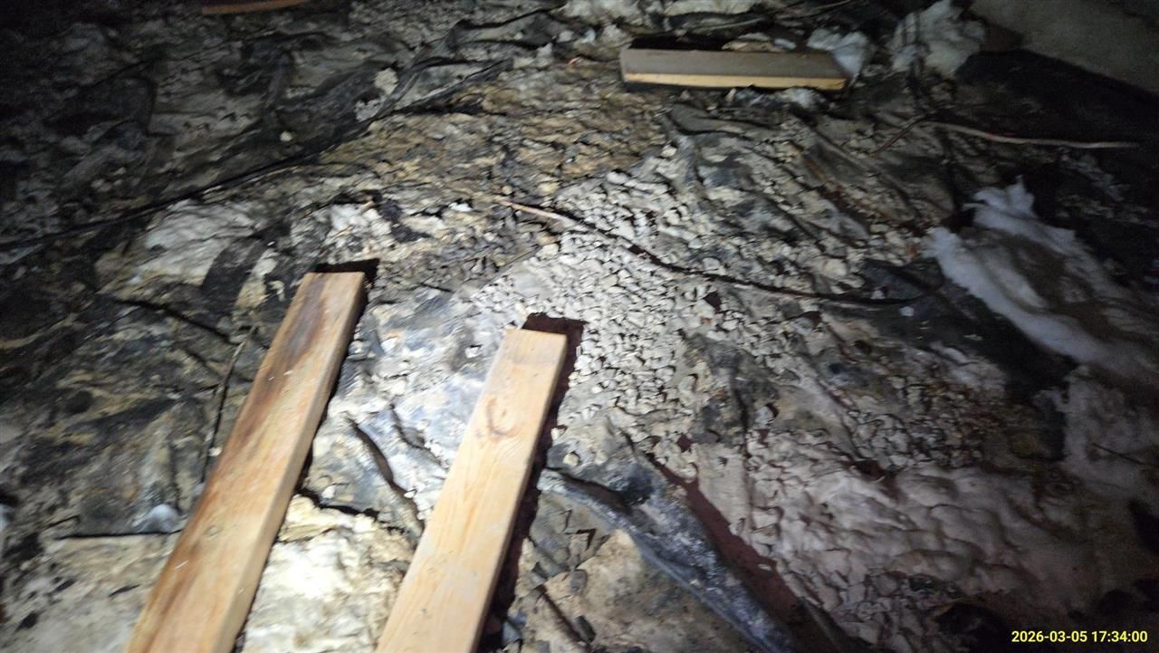 Wooden boards lie on attic insulation, showing dark staining and signs of mold growth.