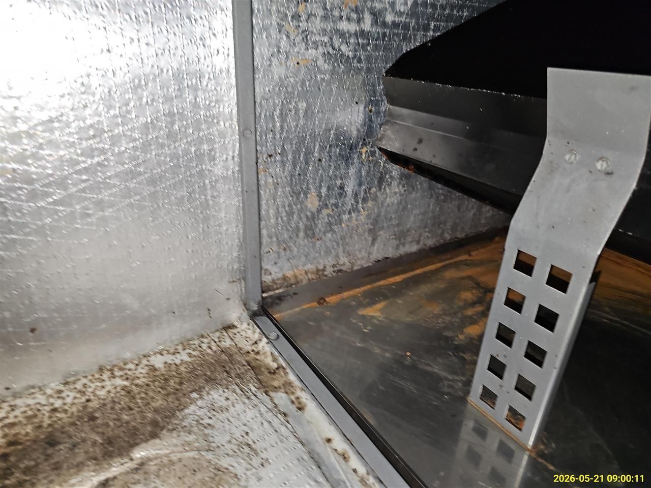 Metal duct or HVAC interior with dusty floor, silver insulation, and a perforated support bracket on the right