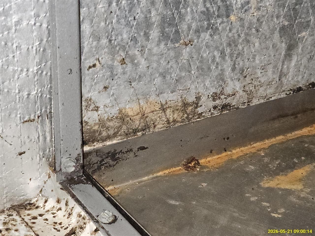 Dirty corner of a metal wall and floor with rust, grime, and debris accumulation