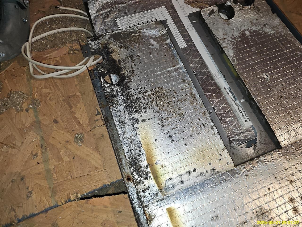 Burned, debris-covered floor with charred metal and a scorched panel indoors