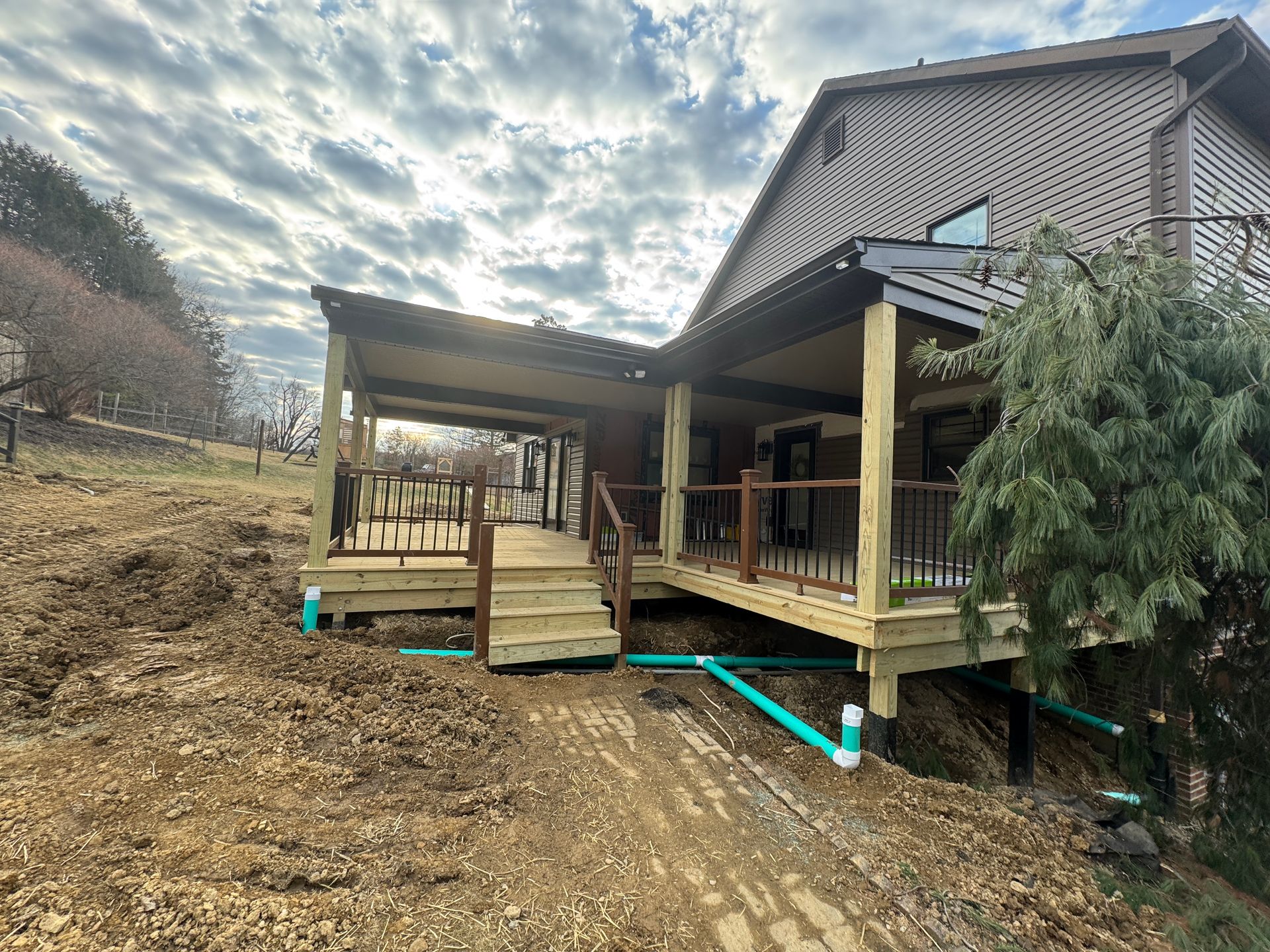 Wooden deck and ramp attached to a house on a hillside. PVC pipes visible. Overcast sky.