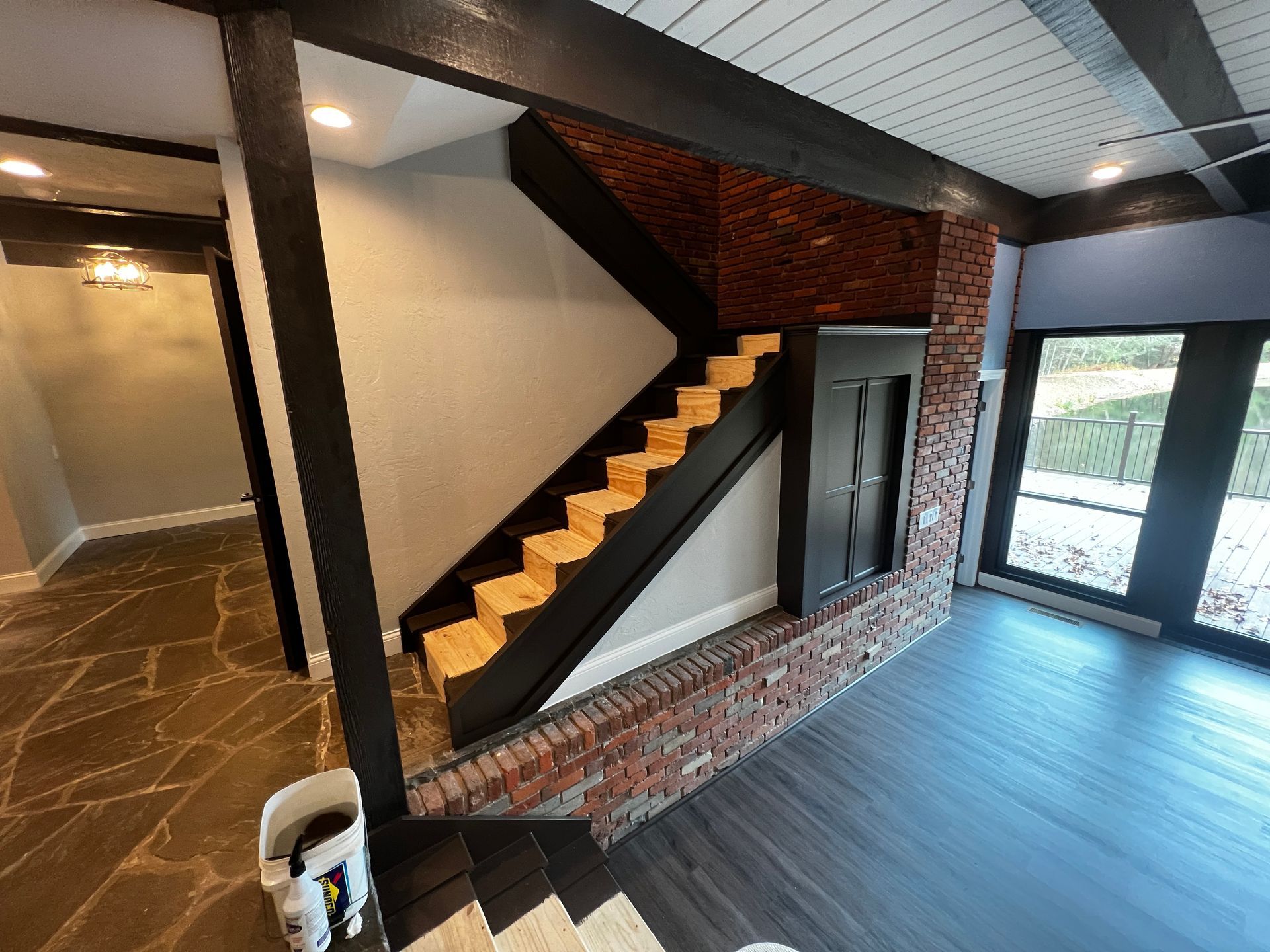 Interior view: Stairs with black trim and wood steps, brick wall, dark wood floors, and large windows.