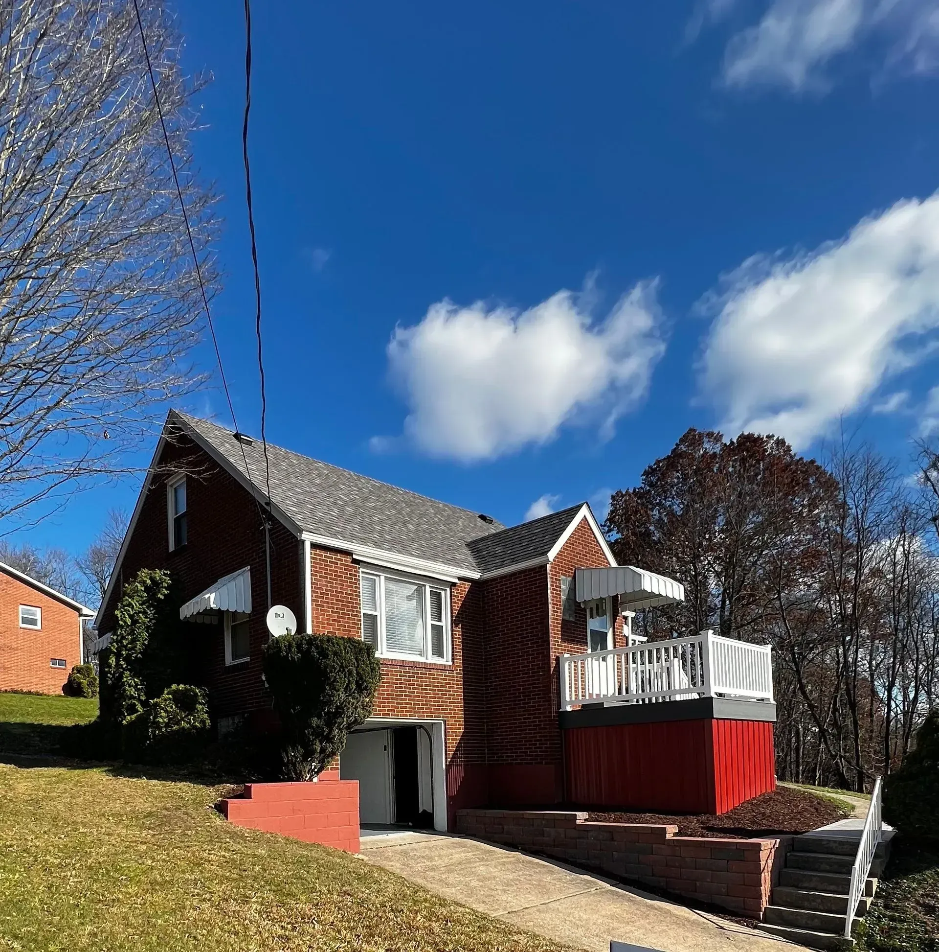 Red brick house with a small balcony and a garage. Overcast blue sky in background.