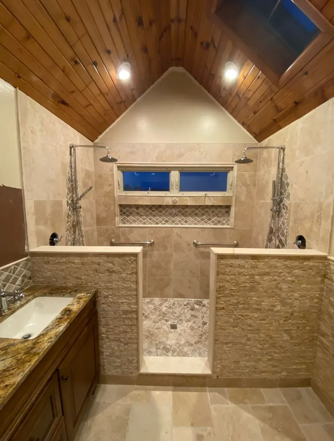 Luxurious bathroom with dual showers and a tub. Beige tile, wooden ceiling, and natural light.