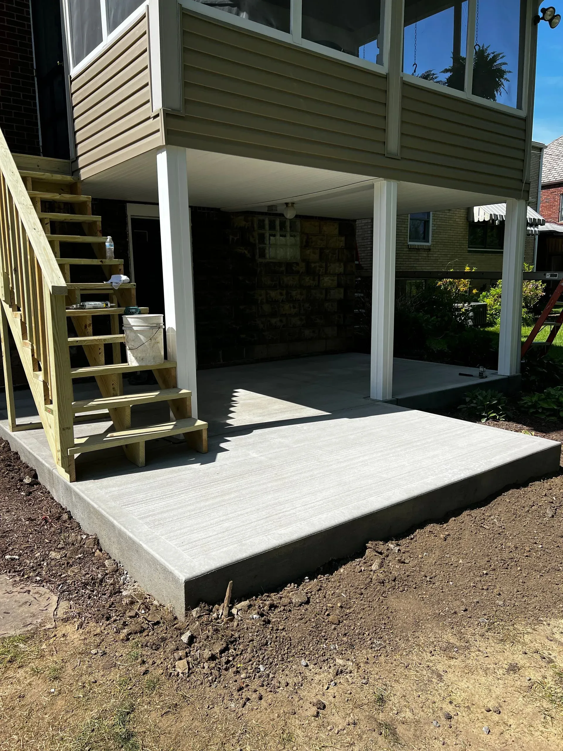 Concrete patio under a screened porch with wooden stairs.