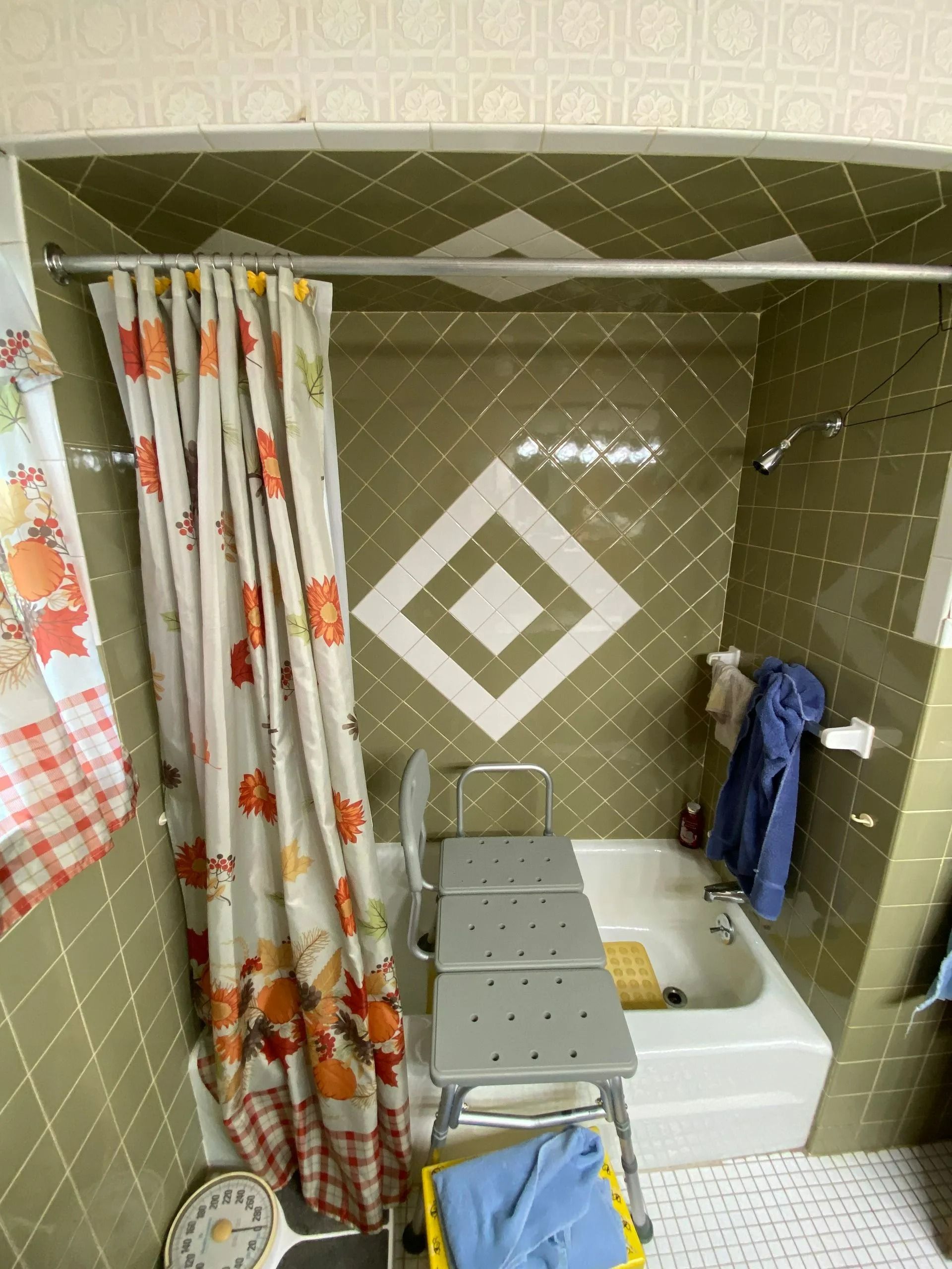 A small bathroom with olive green tiled walls, a shower curtain, and a step stool.