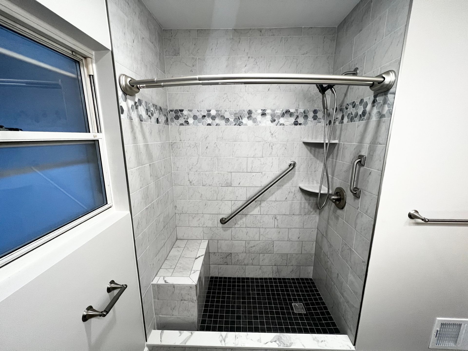Accessible shower with a bench, handrails, and gray and black tiles.