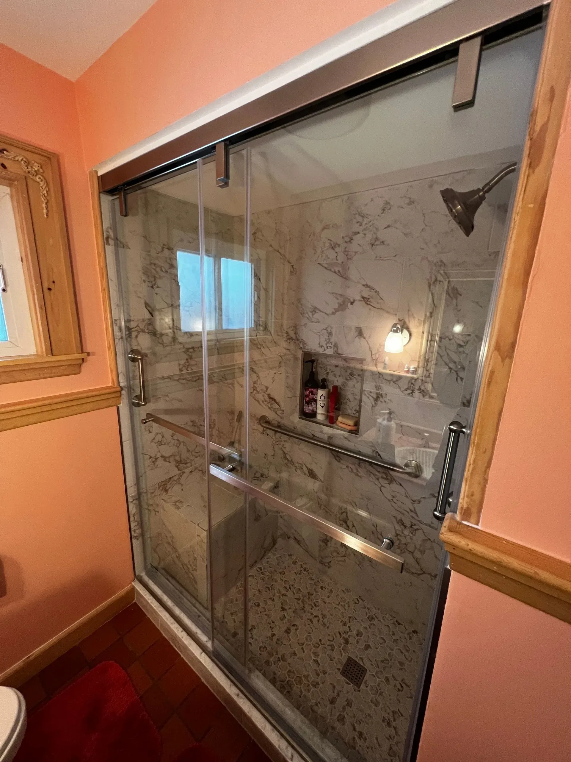 Glass shower enclosure with sliding door, marble tile interior, and bronze hardware.