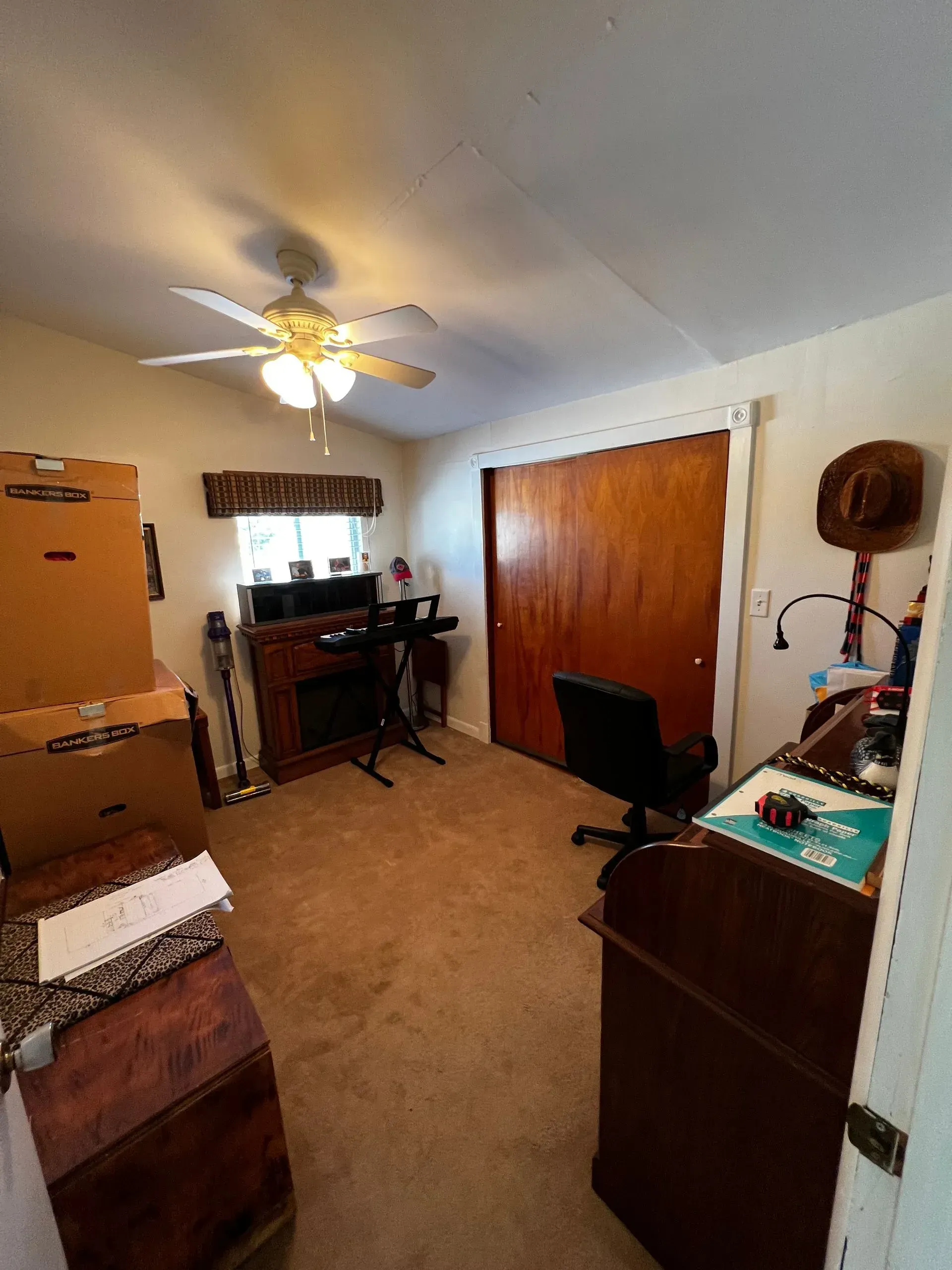 A cluttered home office with boxes, desk, a faux fireplace, and a closet.