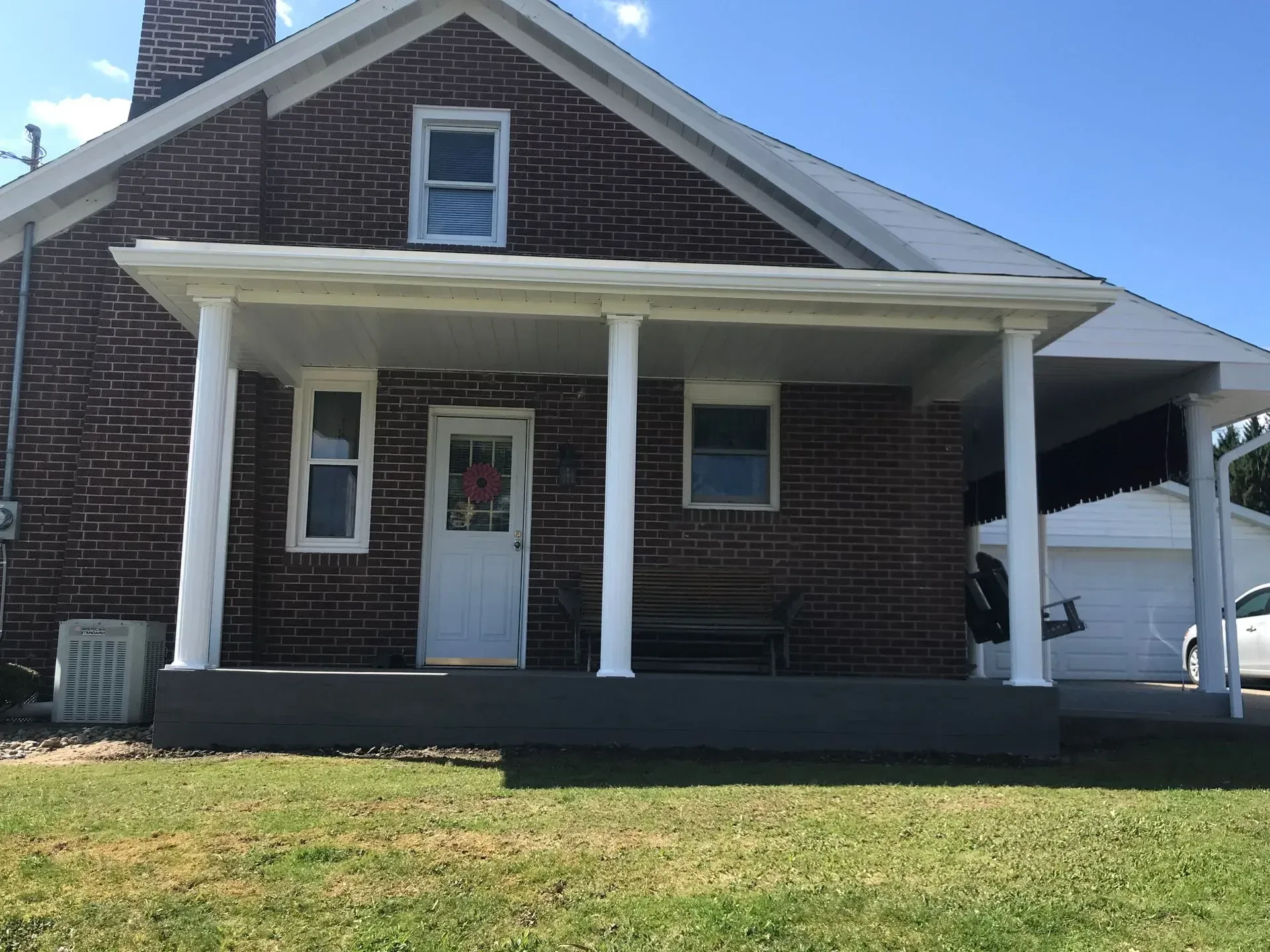 Red brick house with white columns supporting a porch roof, green lawn in front.