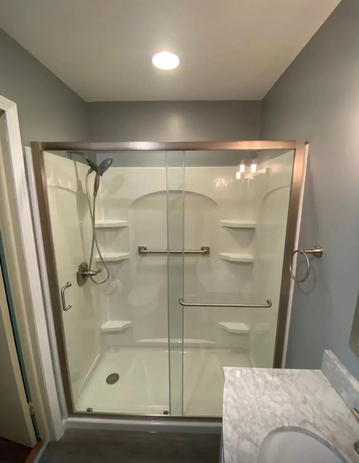 Shower stall with glass doors, built-in shelves, and grab bars. Neutral tones in a bathroom setting.