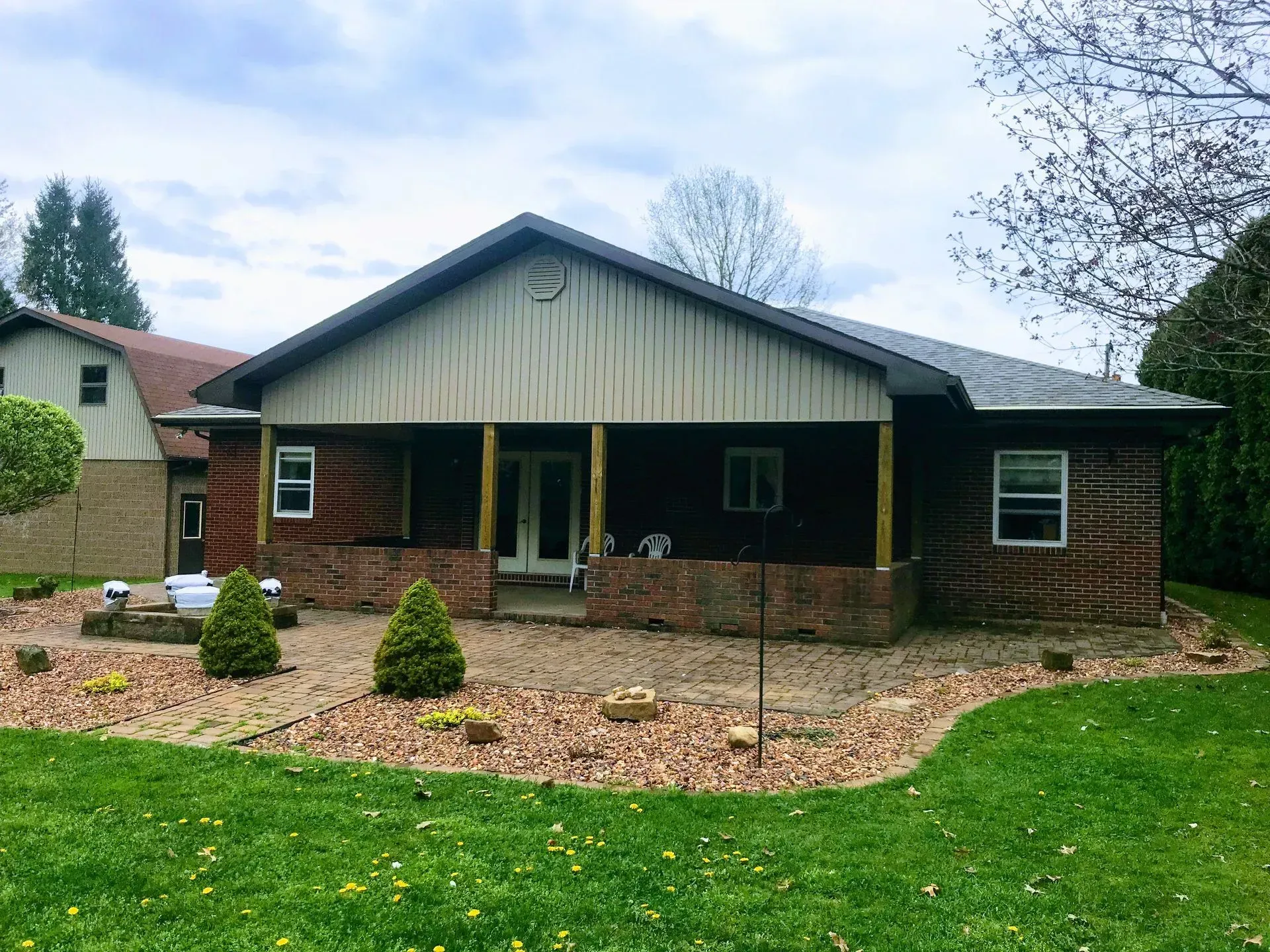 Brick house with a covered porch and small garden in front of a green lawn.