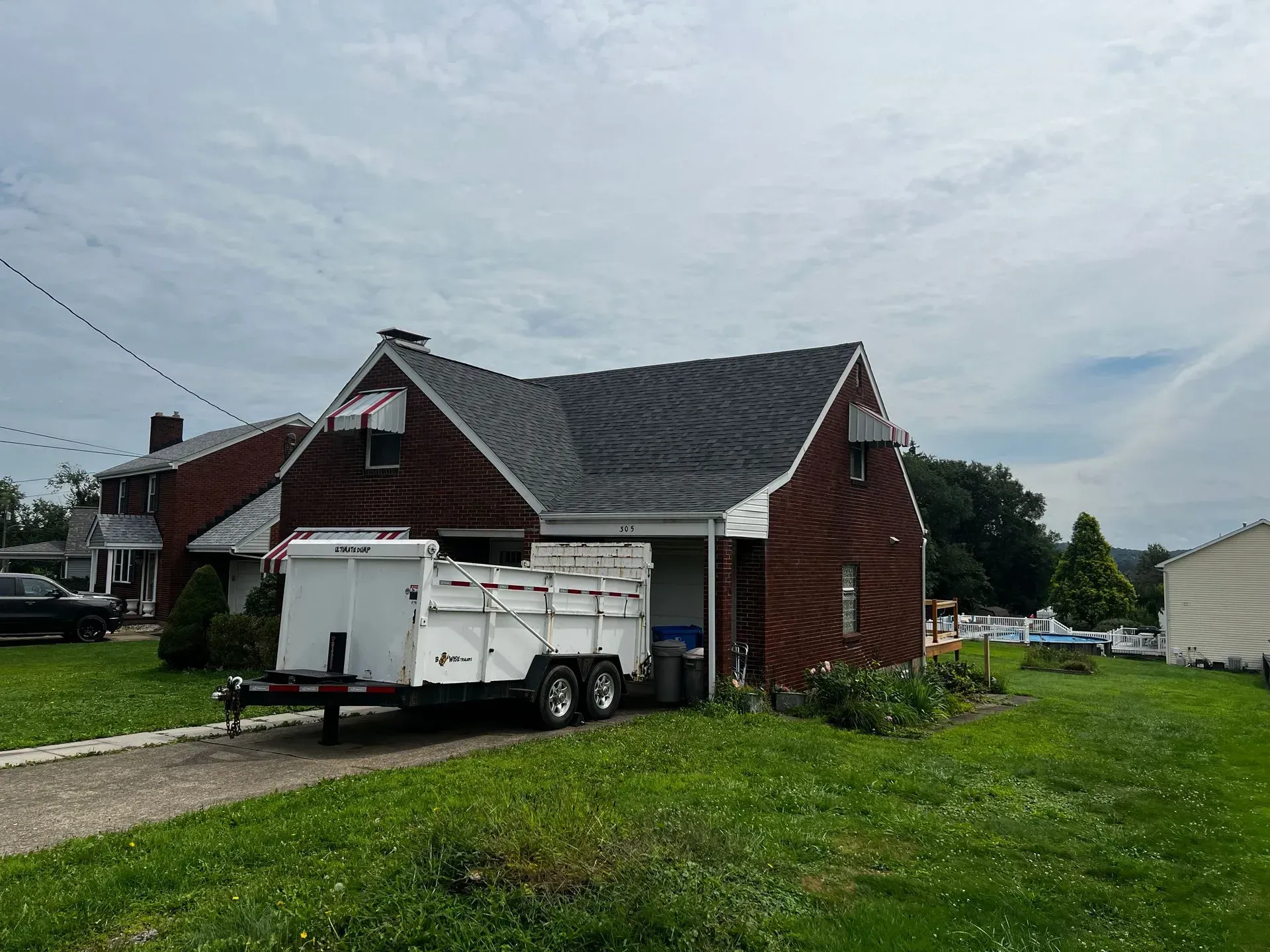 A red brick house with a white trailer parked in front. Overcast sky. Green grass.