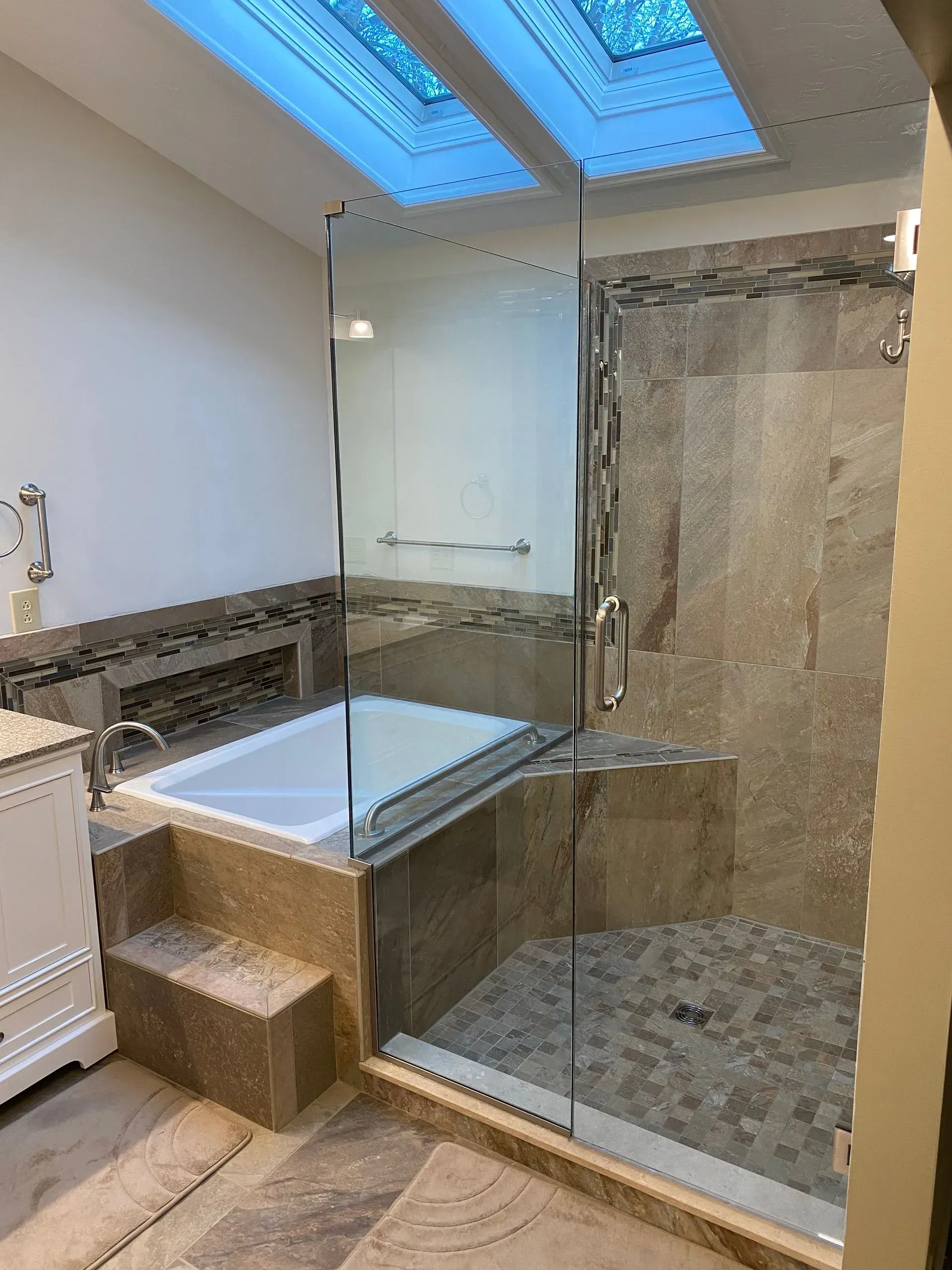 Bathroom with a built-in tub, separate shower, and skylight. Stone tiles and glass shower door.