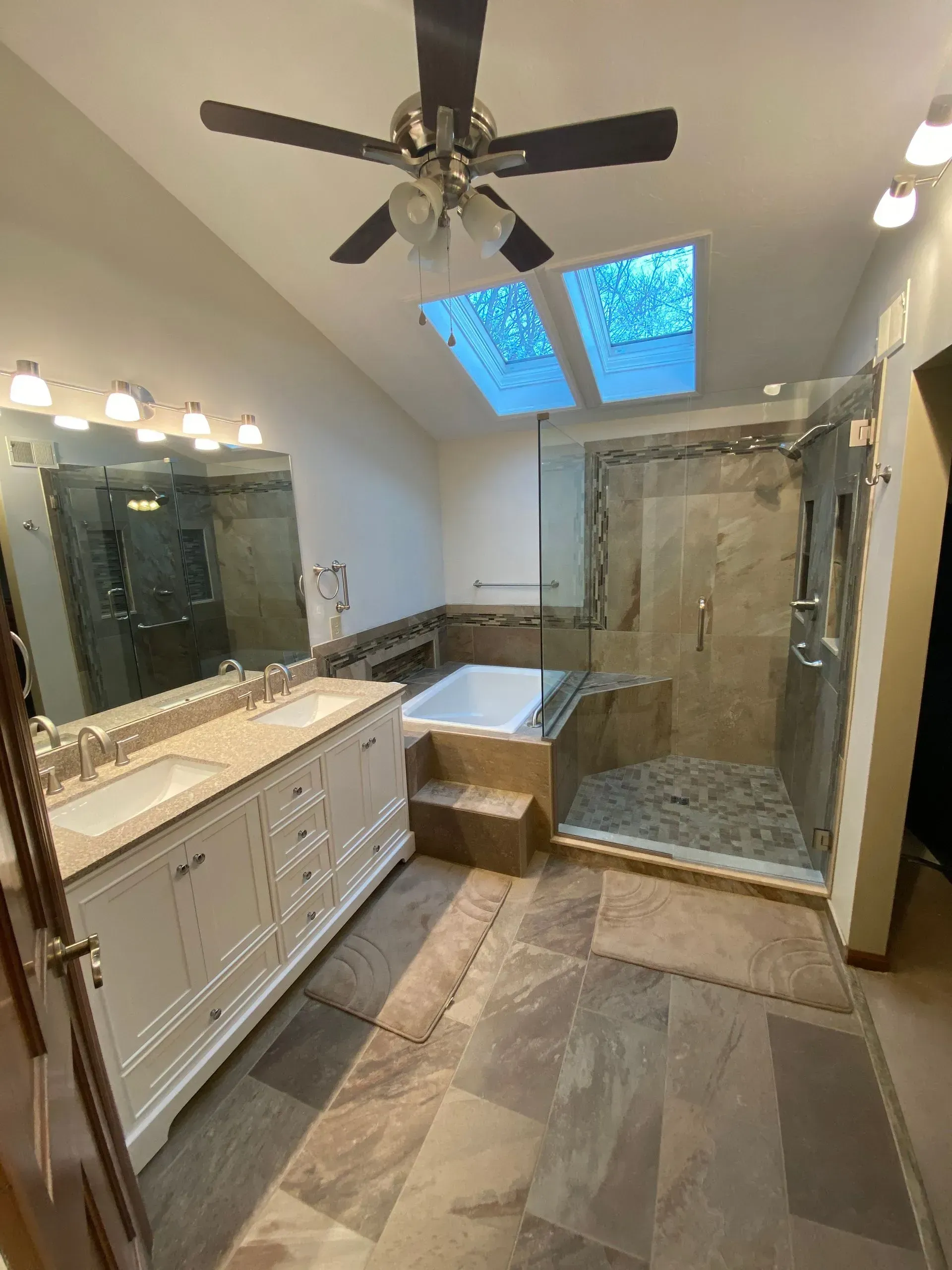 Spacious bathroom with beige tile floors and walls. Features a shower, tub, double vanity, and skylights.