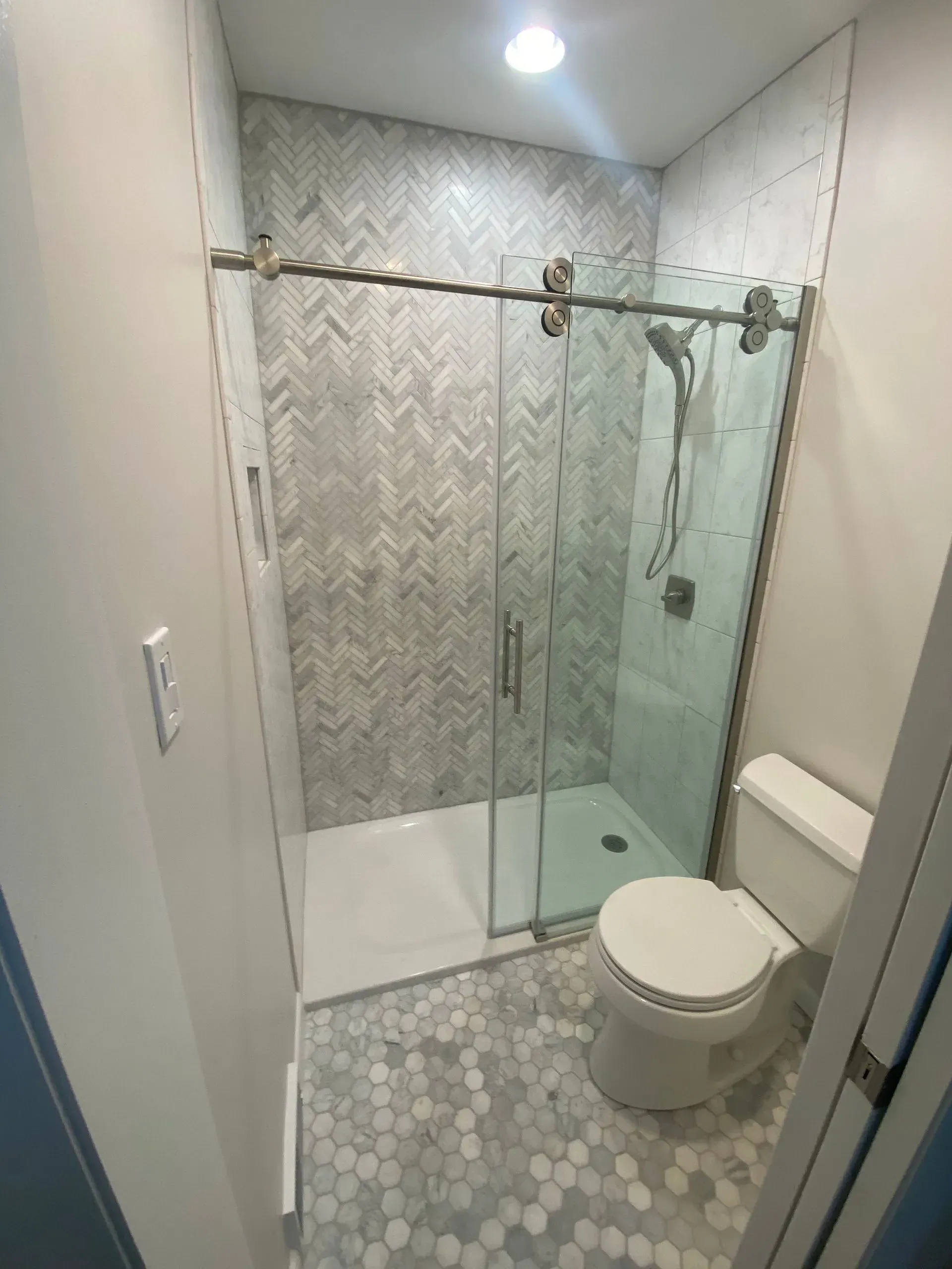 Small modern bathroom with glass shower, patterned tile, and white toilet.