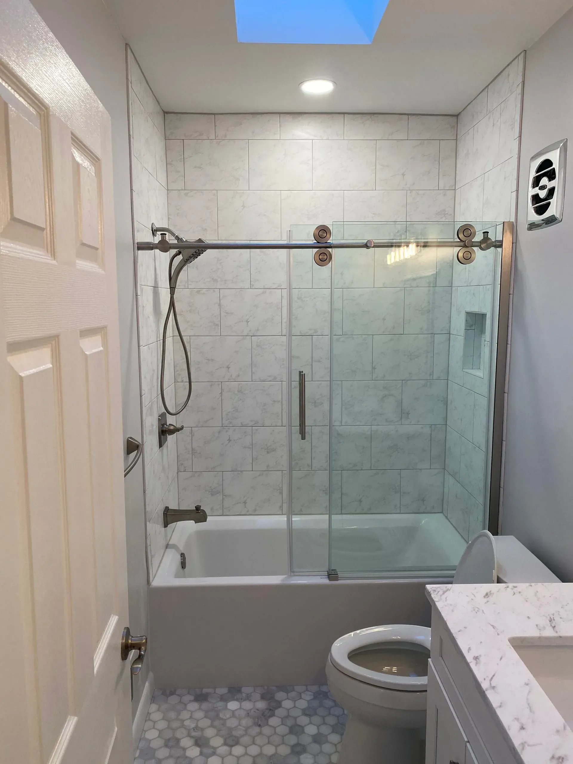 Bathroom with white tile, glass shower door, toilet, vanity, and skylight.