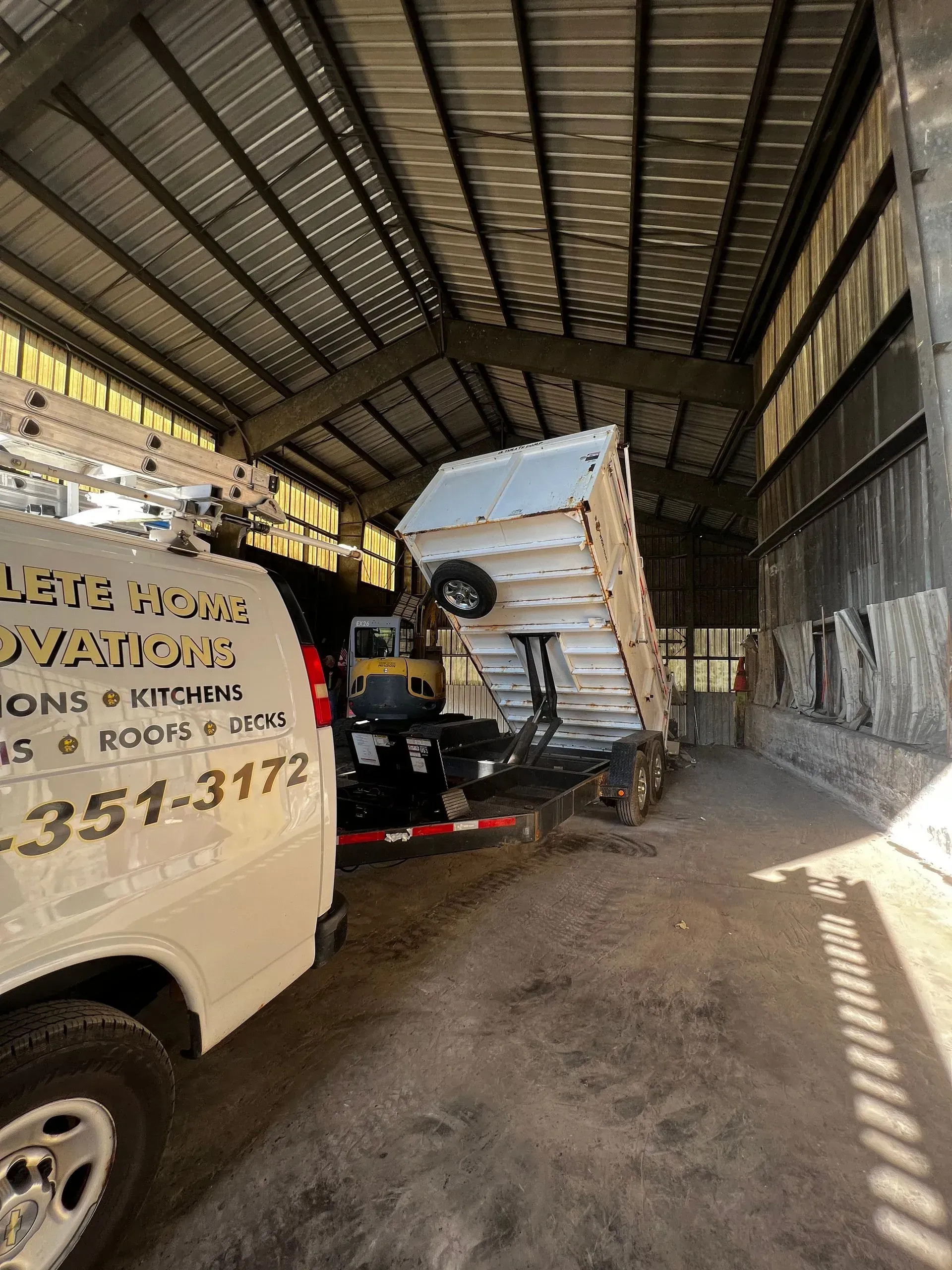 A dump truck is inside a building with a white work van parked next to it.