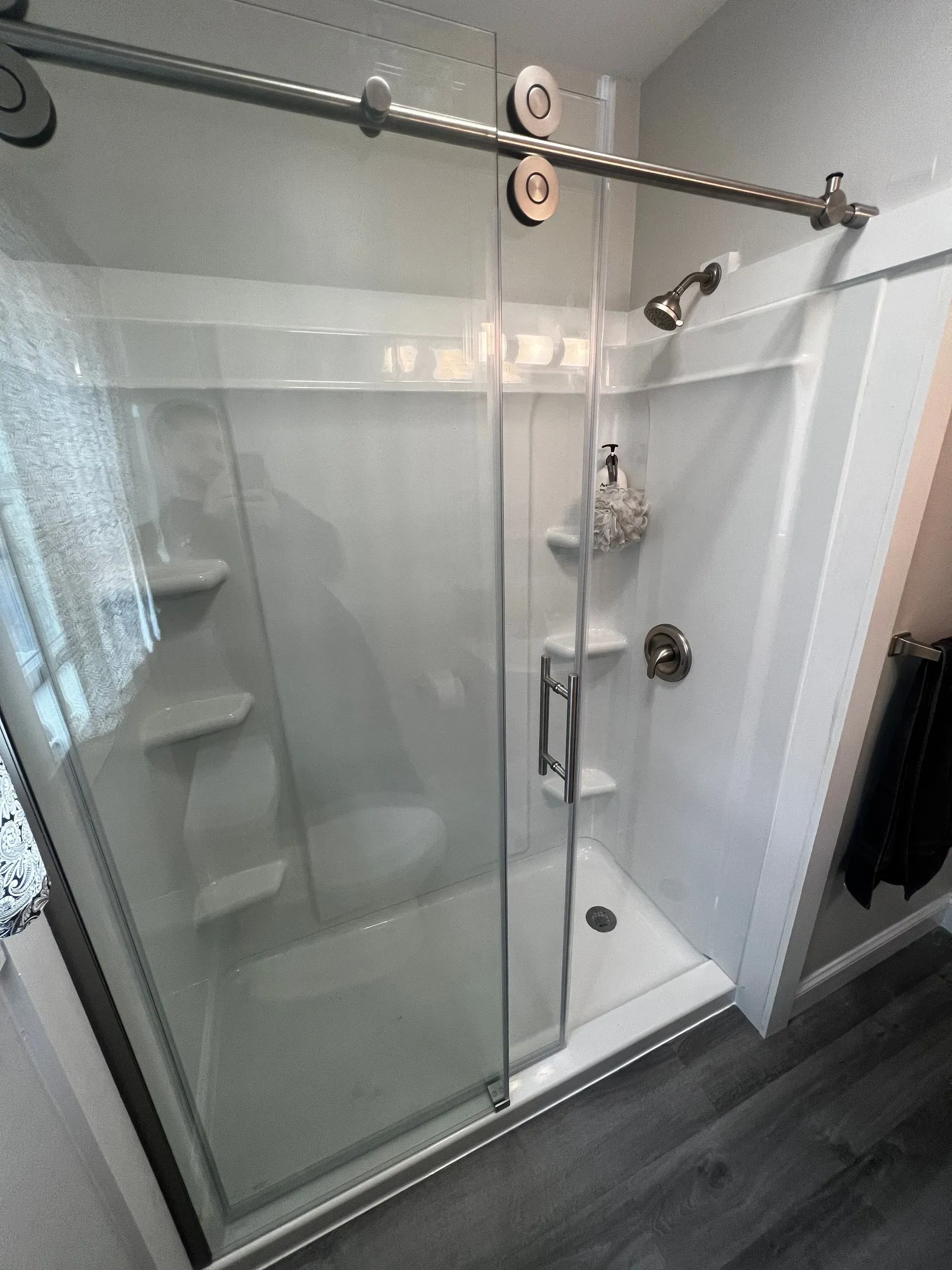 Glass-door shower with sliding door on a white and gray tiled wall. Silver shower fixtures and shelves.