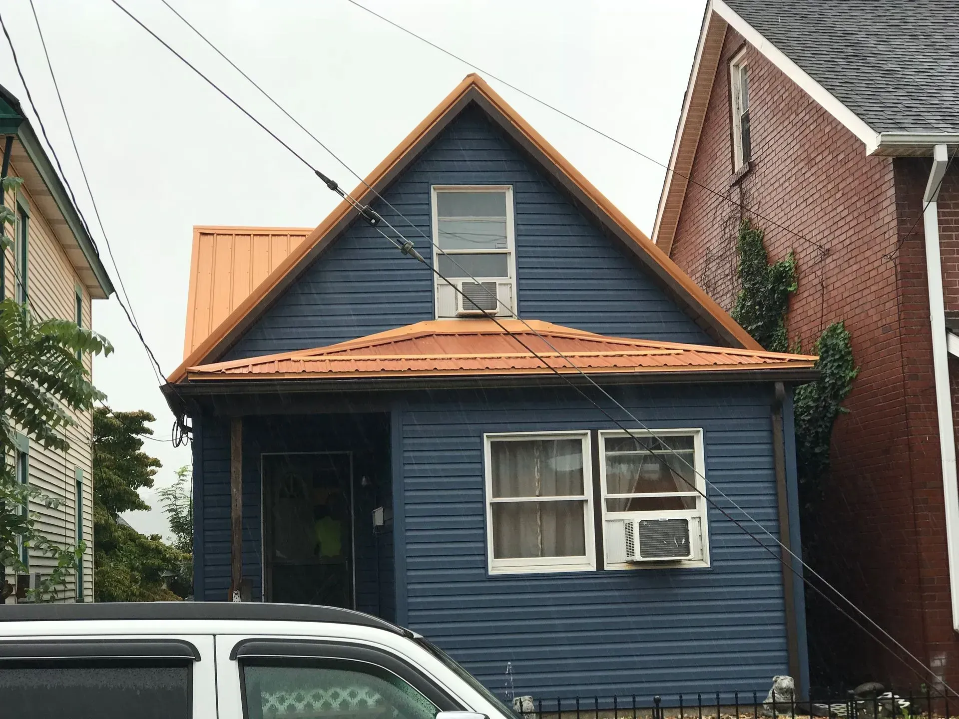 Blue house with orange roof, two windows, and an air conditioner.