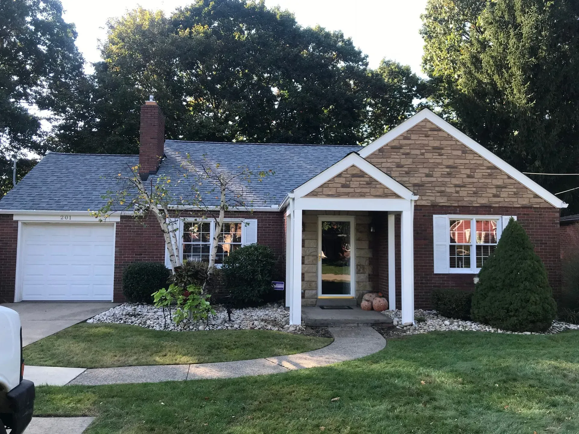 Brick bungalow home with tan stone facade, white trim, grey roof, and a small front yard.