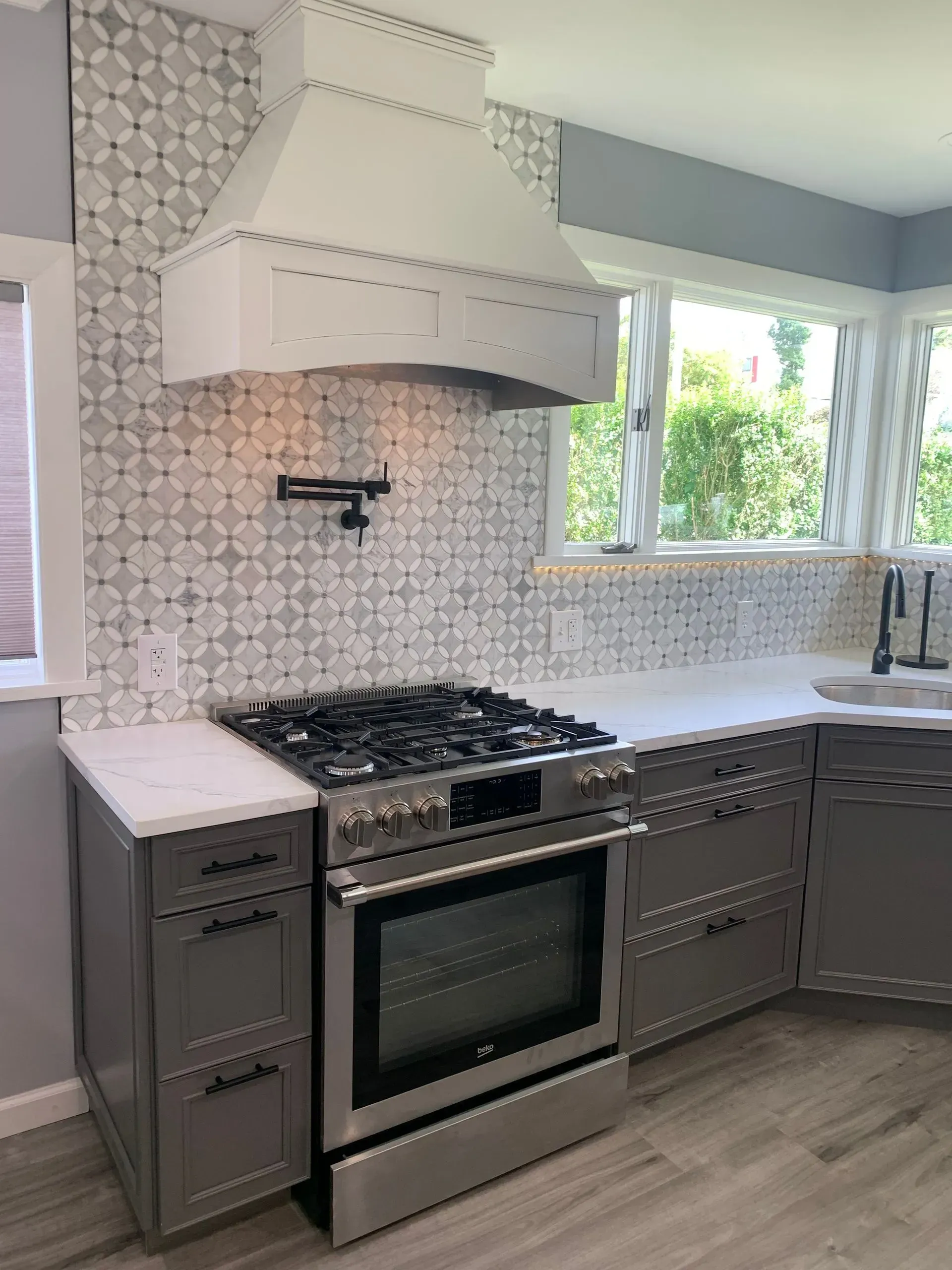 Gray kitchen with stovetop, range hood, tile backsplash, and cabinets.