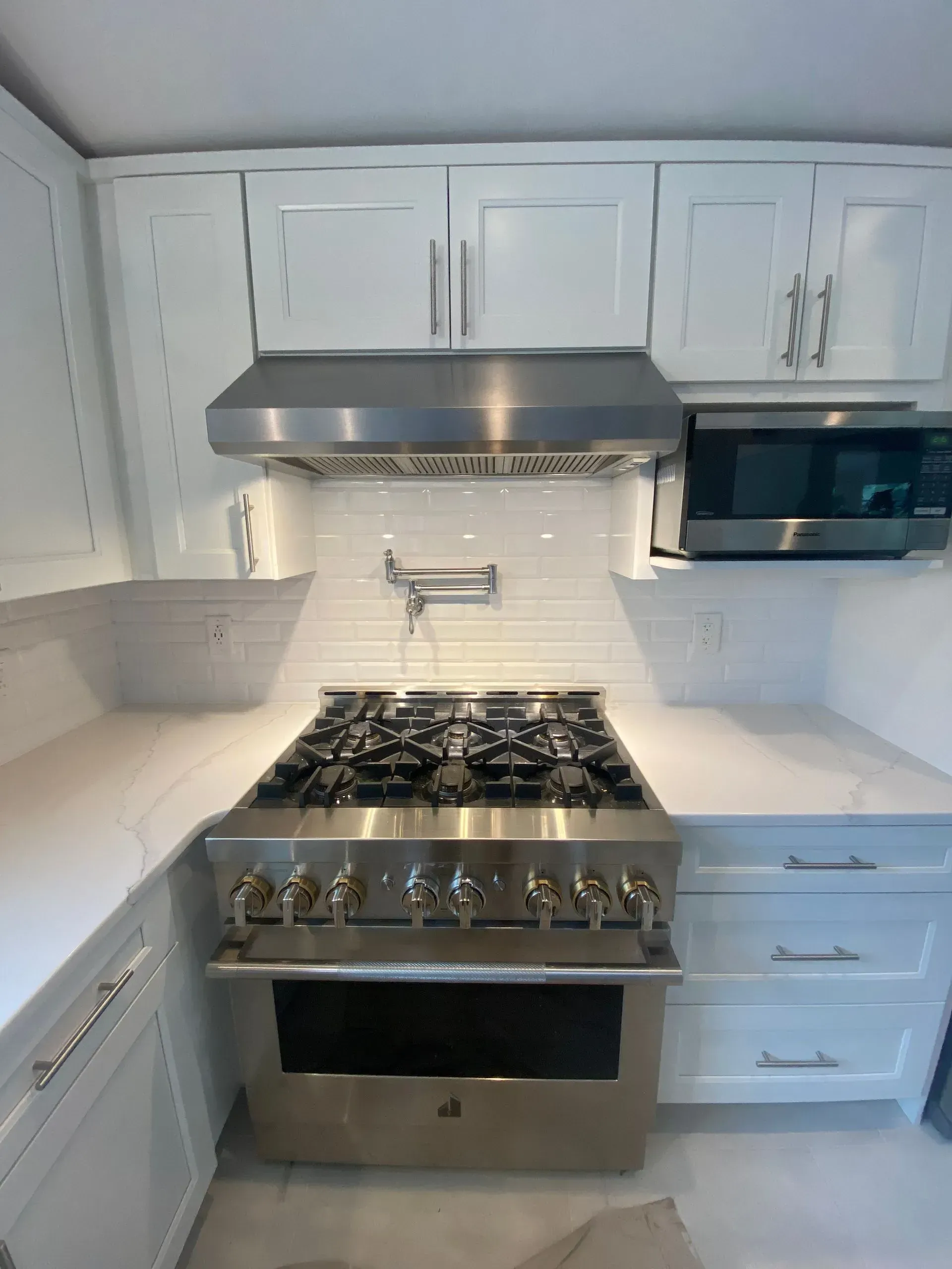 Stainless steel gas range in a white kitchen with white cabinets, a range hood, and microwave.