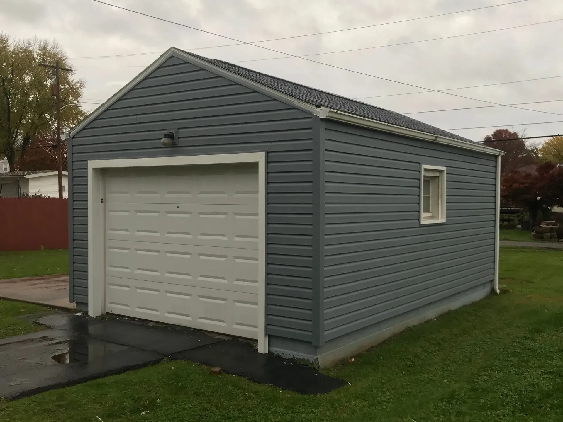 Gray garage with white door and window, on a green lawn under a cloudy sky.