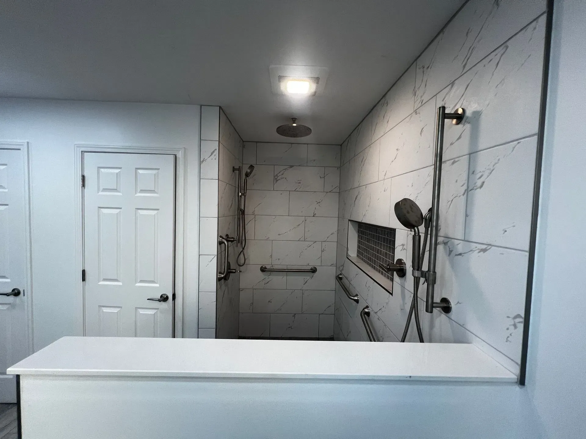 Bathroom with tiled shower, grab bars, and a raised countertop.