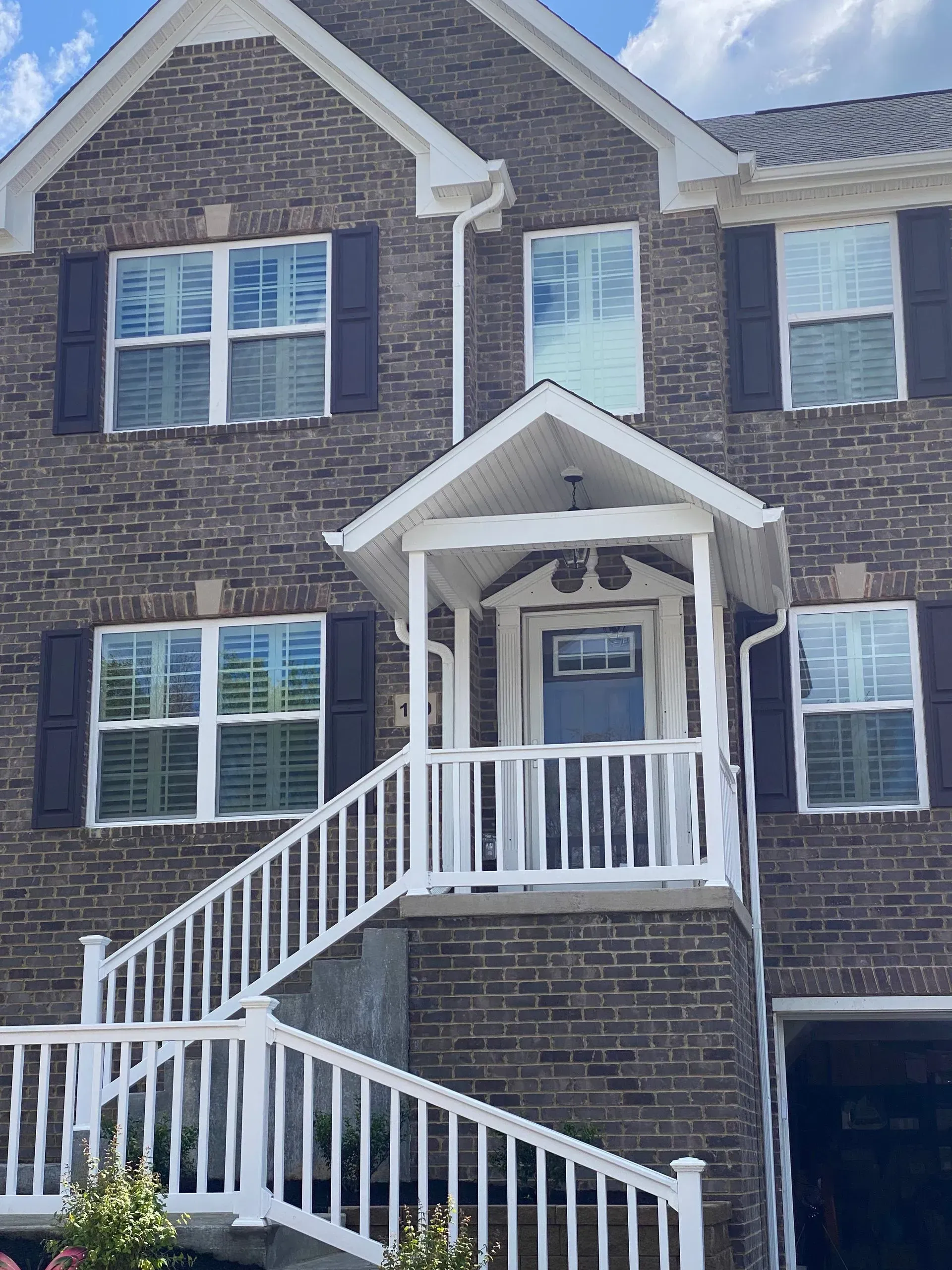 Two-story brick house with white porch, stairs, and dark brown shutters.