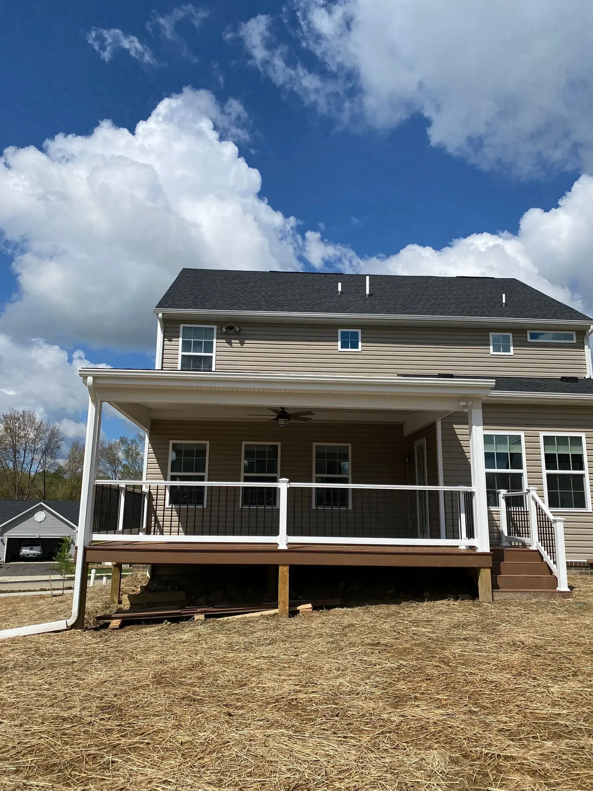 Back of a two-story beige house with a covered porch and deck. Blue sky with white clouds.