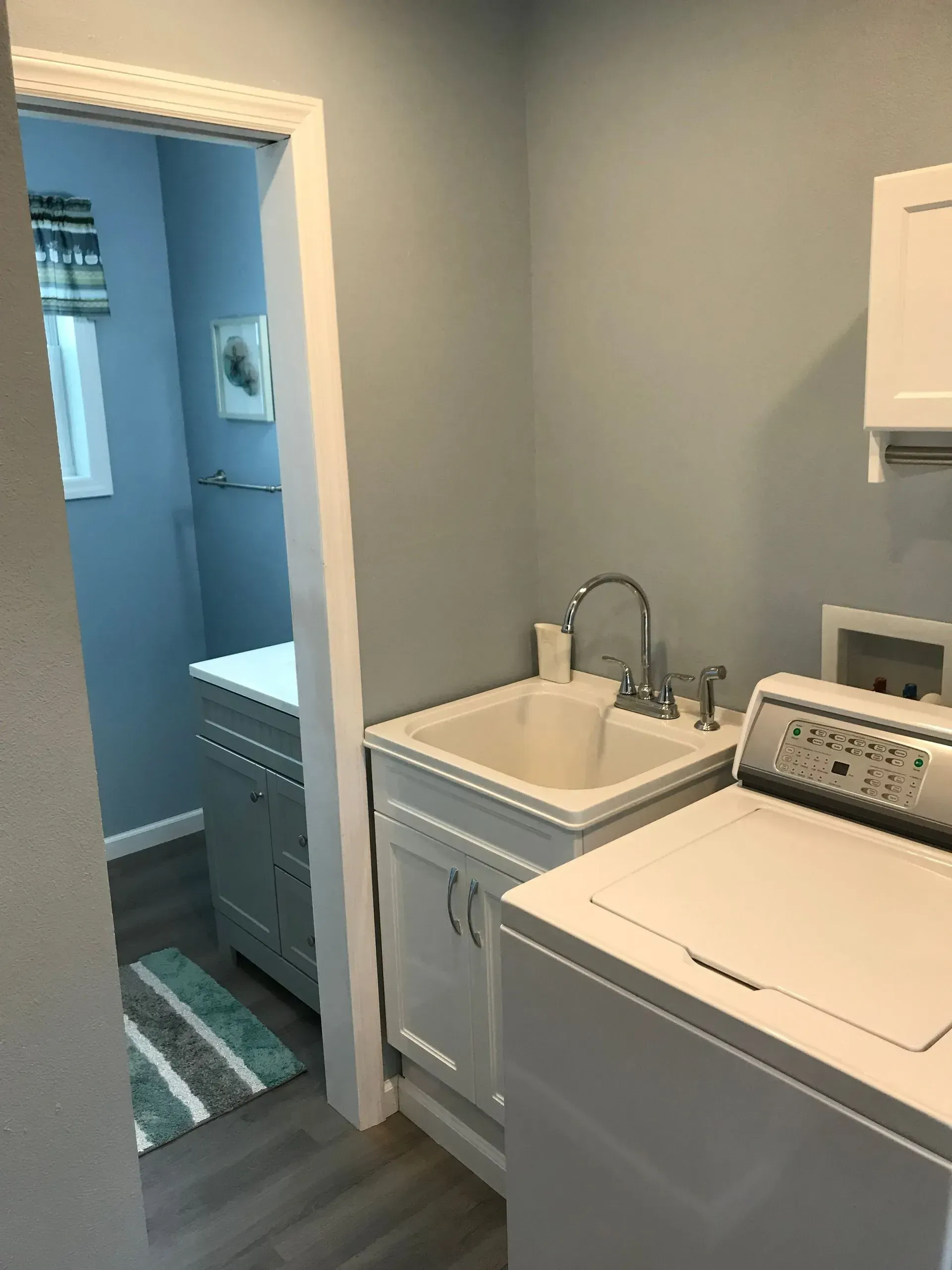 Laundry room with a washing machine, sink, and doorway to a blue-walled room.
