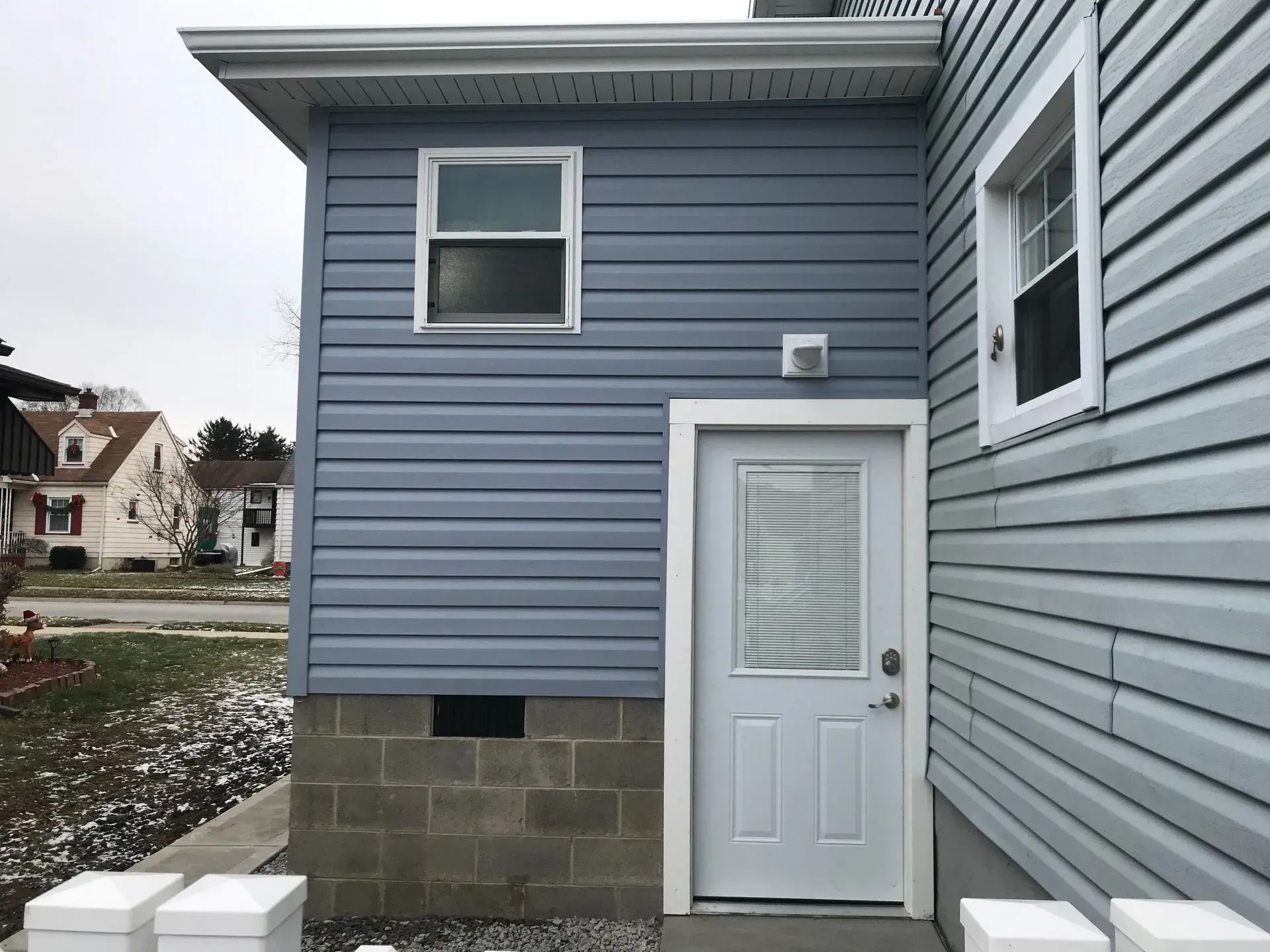 Blue-sided exterior with a white door, window, and trim. Concrete block foundation.