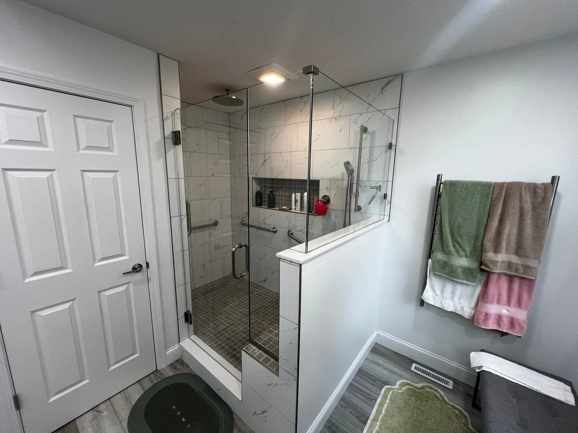 Bathroom with walk-in shower, glass door, white walls, and towels hanging on a rack.