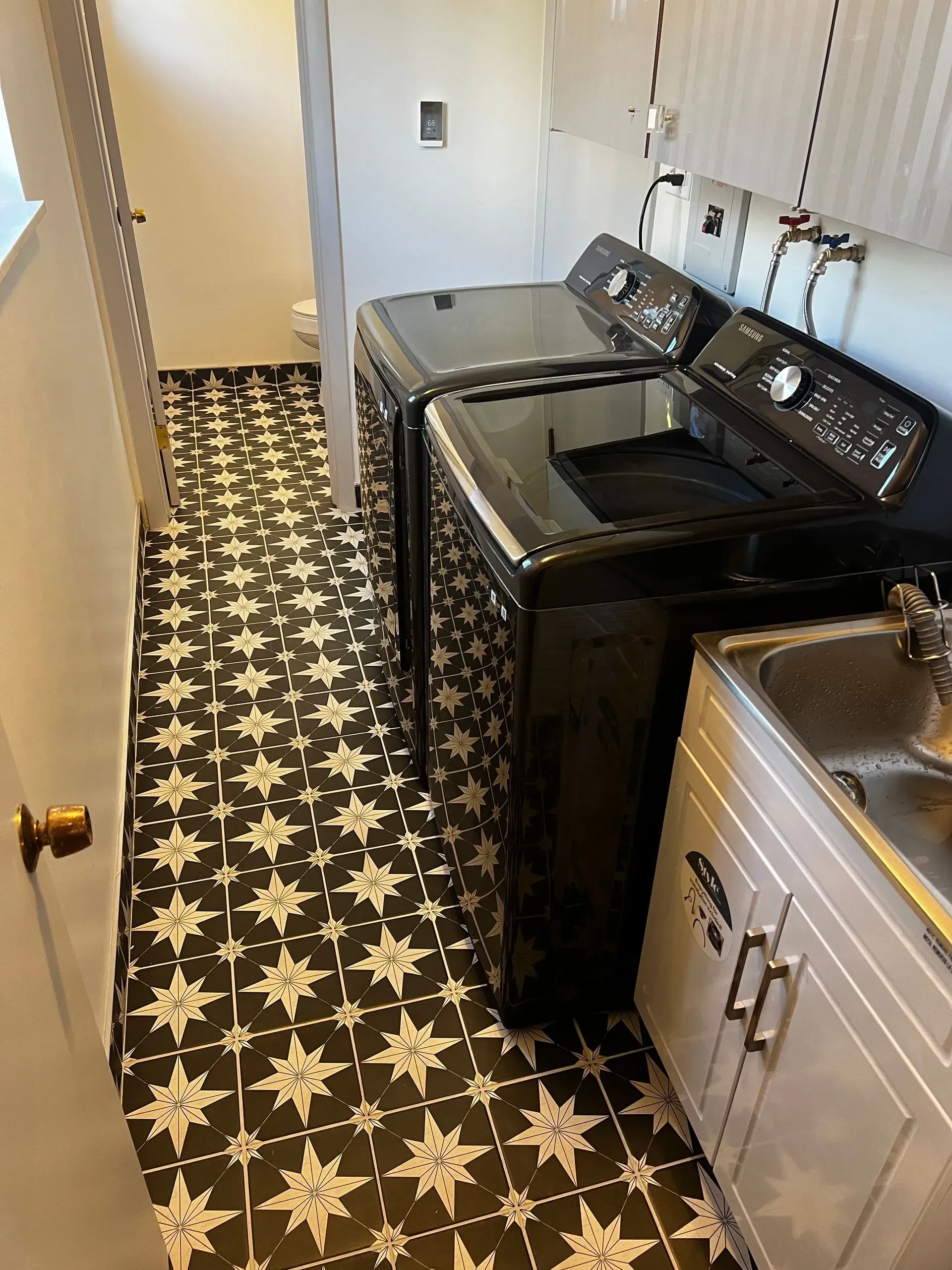 Laundry room with black appliances, white sink, and patterned black and white floor tiles.