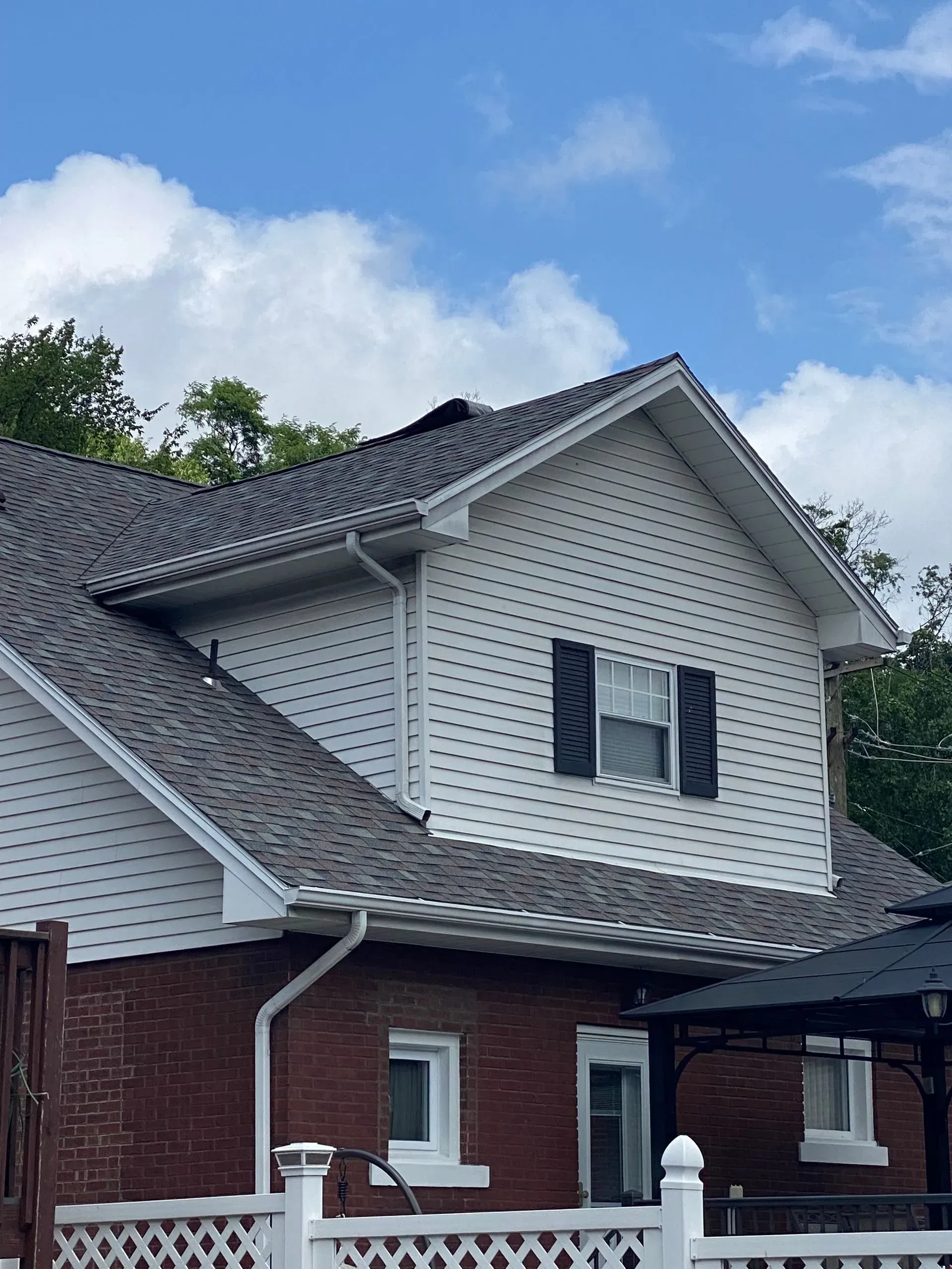 Two-story house with white siding and a dark roof under a blue sky.