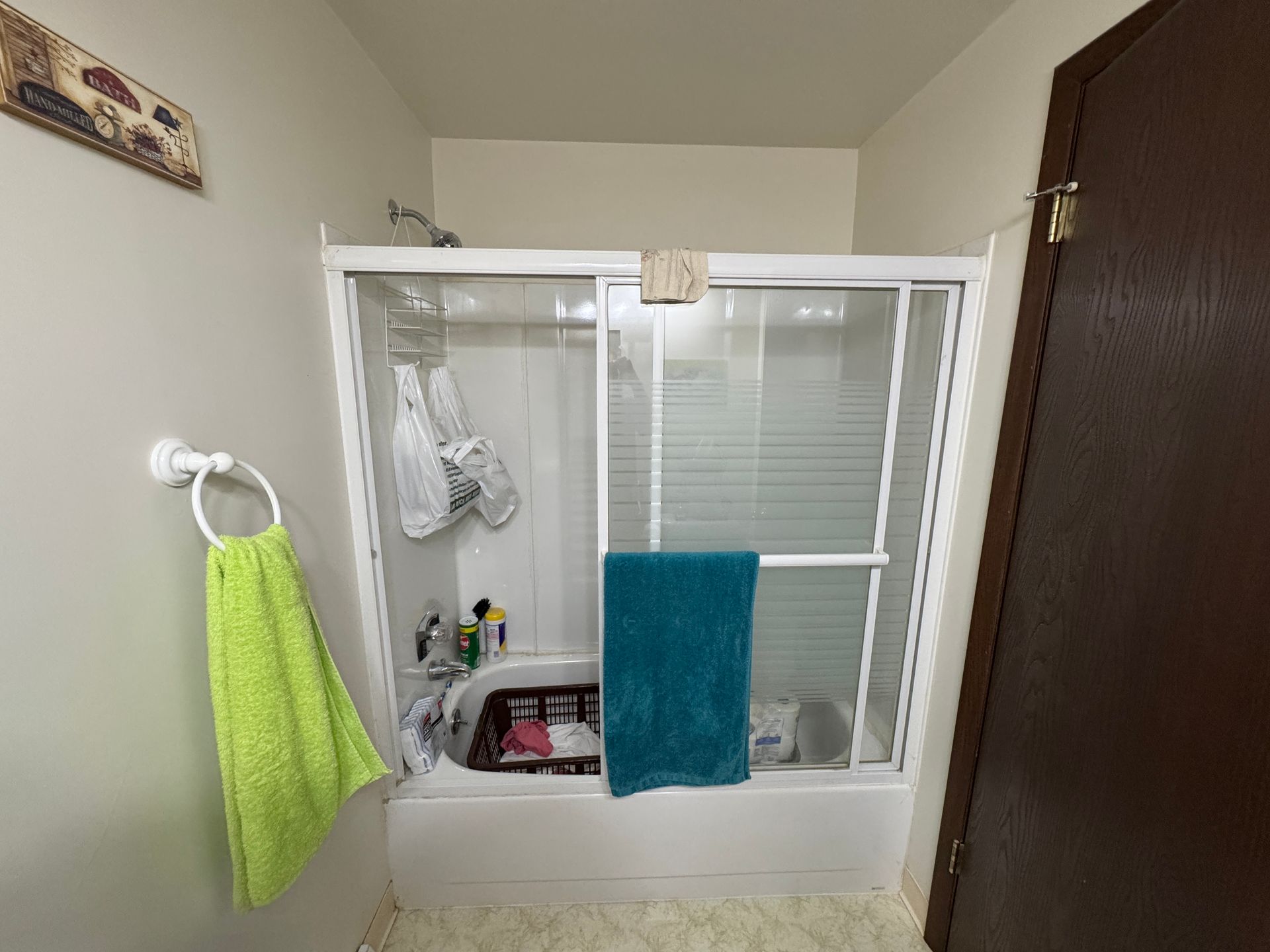 Bathroom with white tub, sliding shower door, green and blue towels.