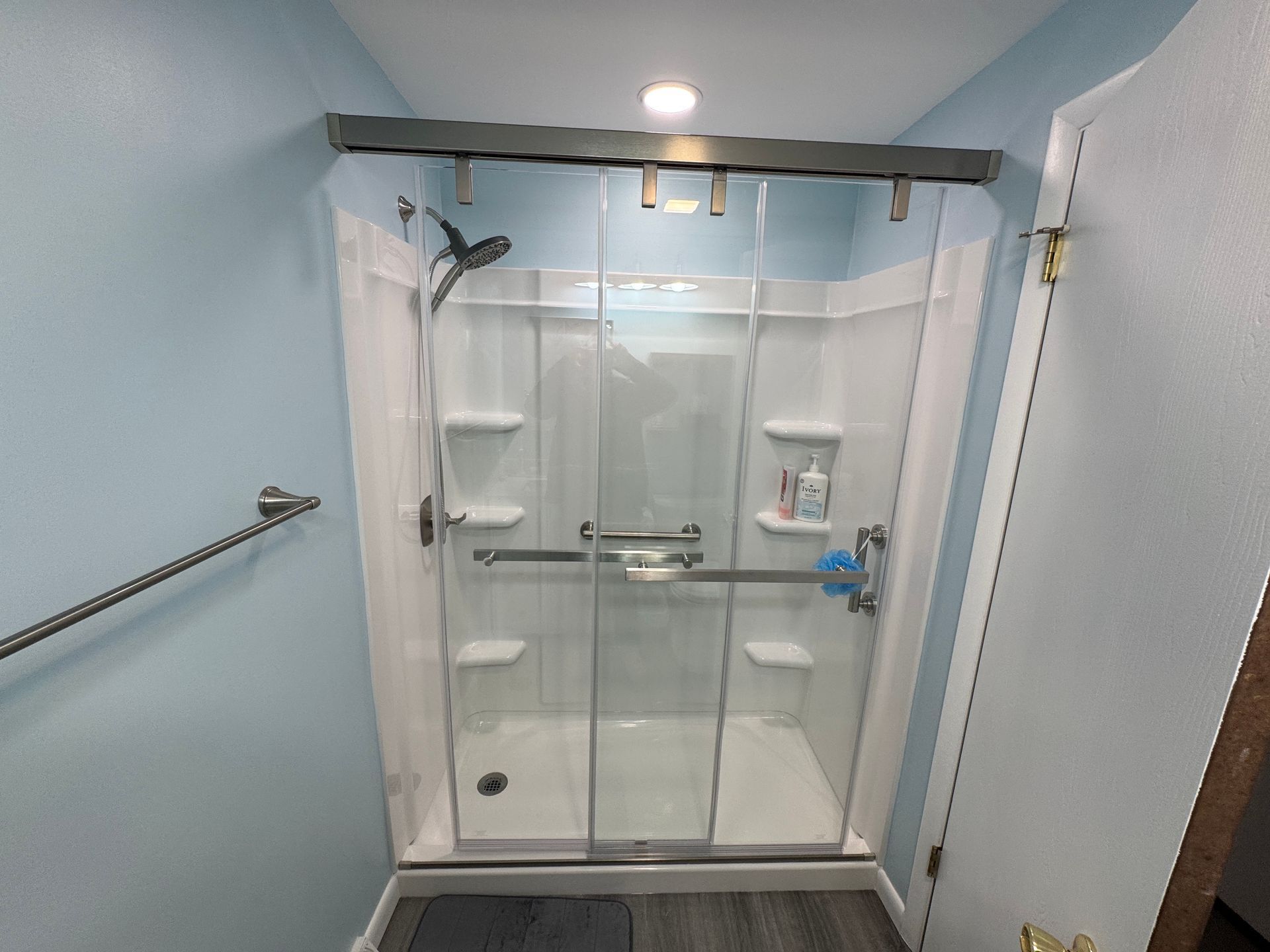 Shower stall with grab bars and sliding glass doors; blue walls, white fixtures, and gray flooring.