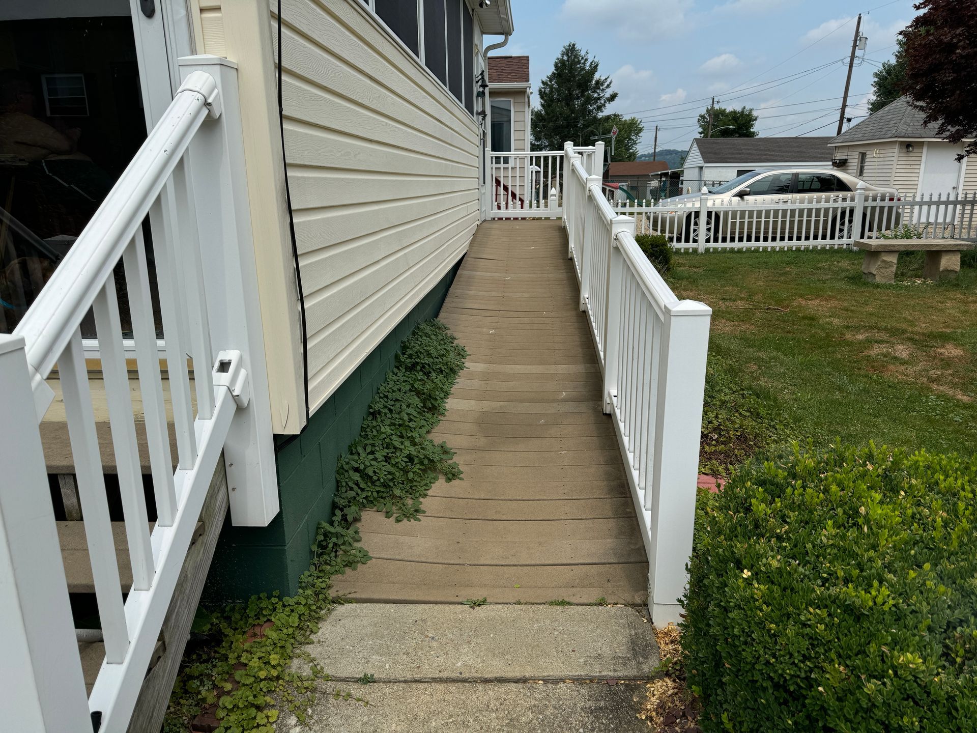 Concrete ramp with white handrails leading to a building's entrance. Green plants line the ramp's base.