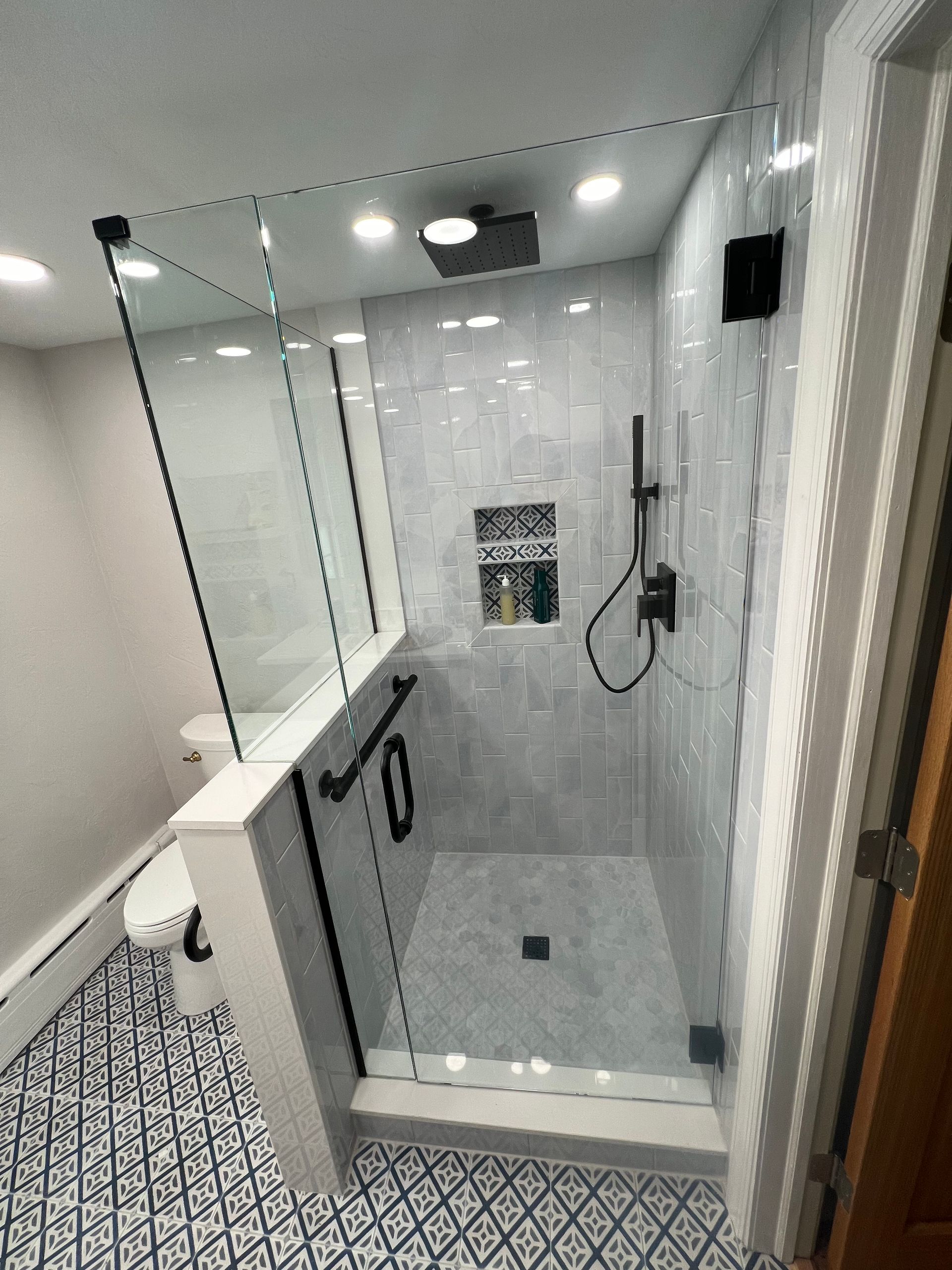 Modern, tiled shower with glass doors, black fixtures, and a low curb; adjacent toilet.