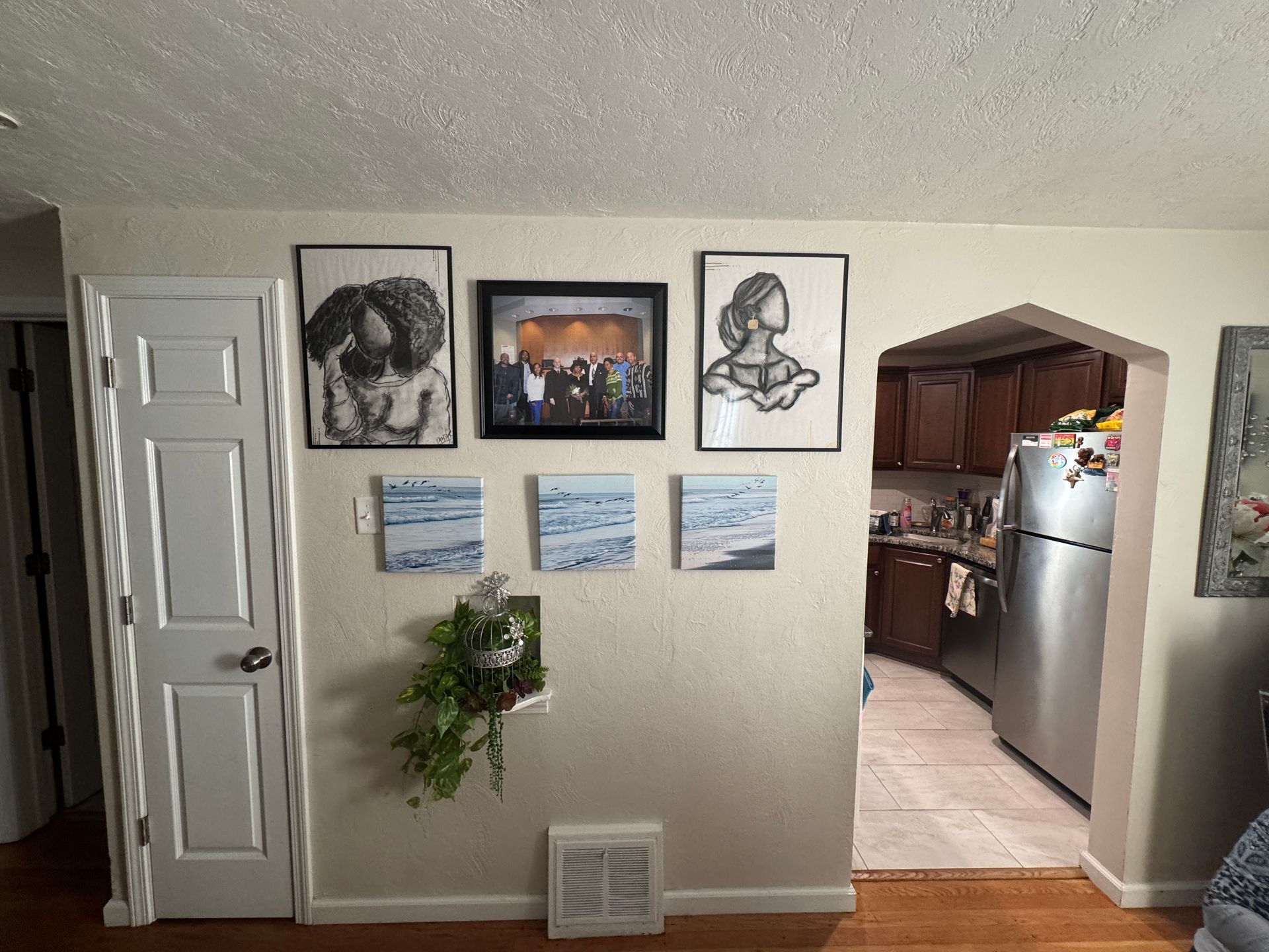 Wall with framed artwork, arched doorway to kitchen with stainless steel refrigerator.