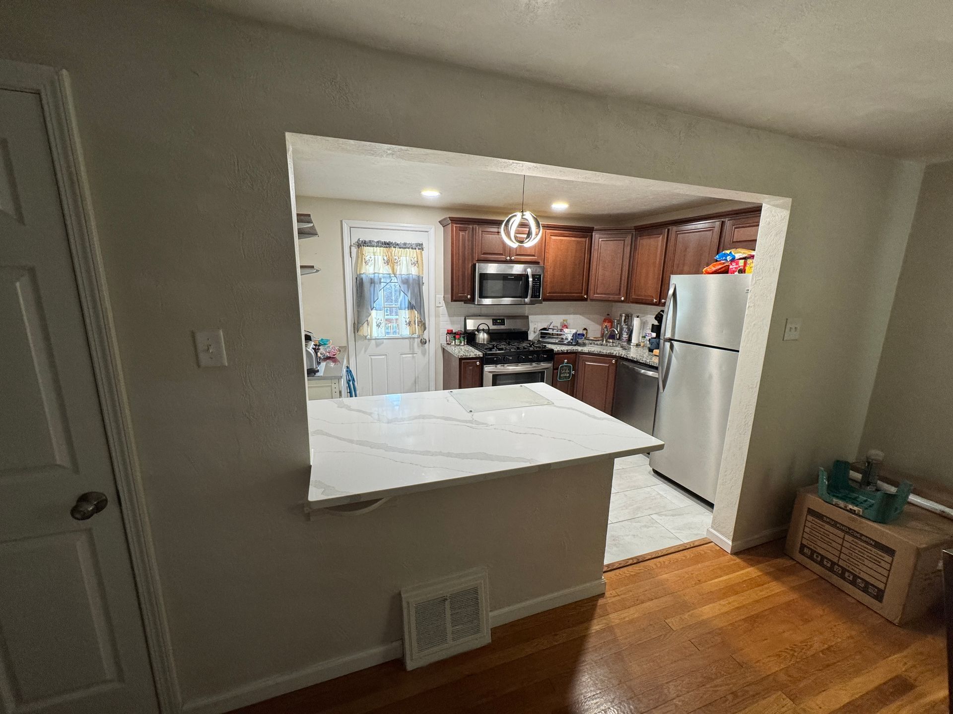 A pass-through kitchen area with countertop and cabinets; stainless steel appliances. Hardwood floors, neutral walls.