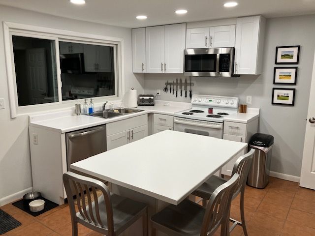 White kitchen with stainless steel appliances, a center island, and bar stools.