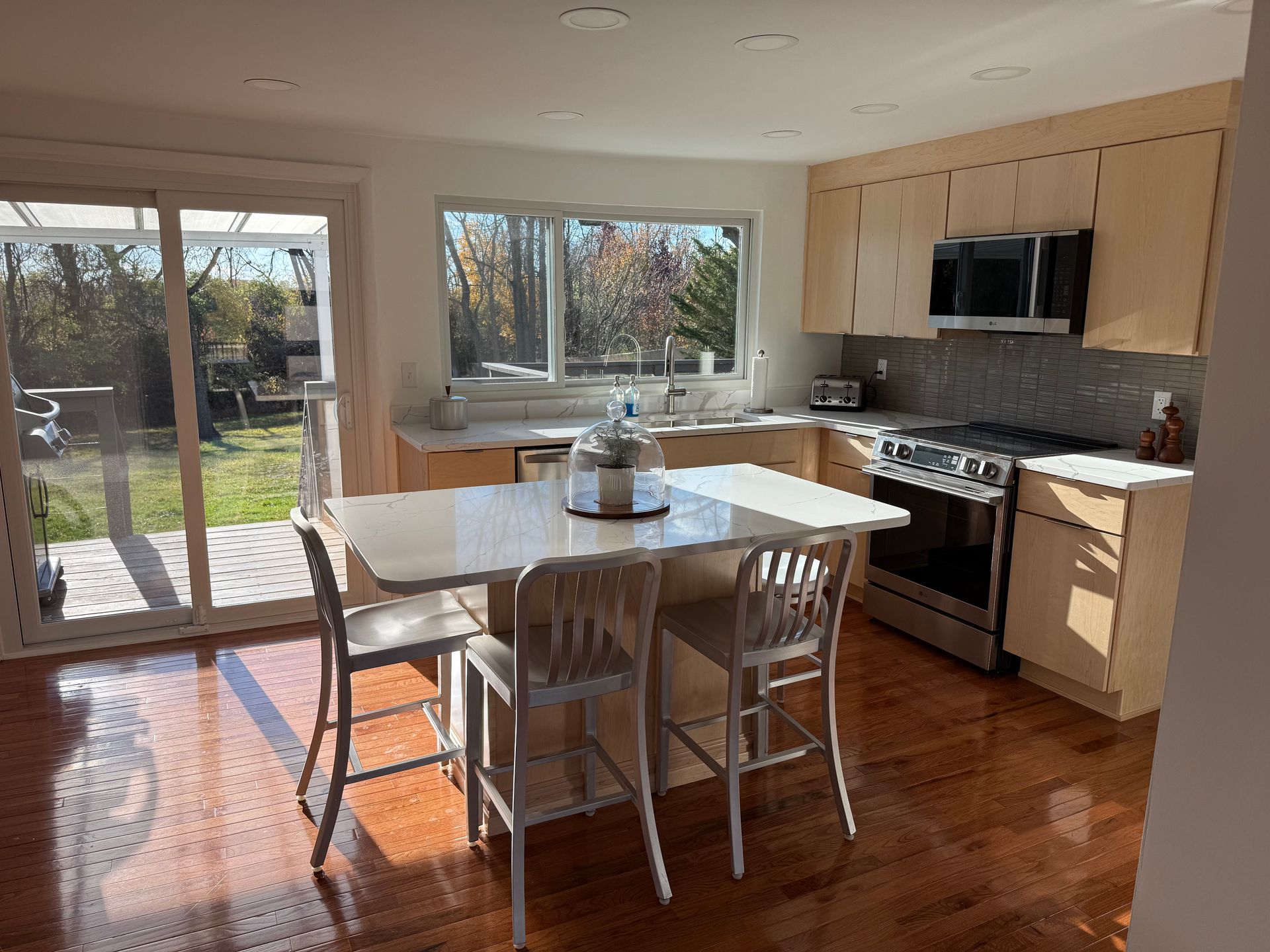 Kitchen with light wood cabinets, stainless steel appliances, and a breakfast bar overlooking a backyard.